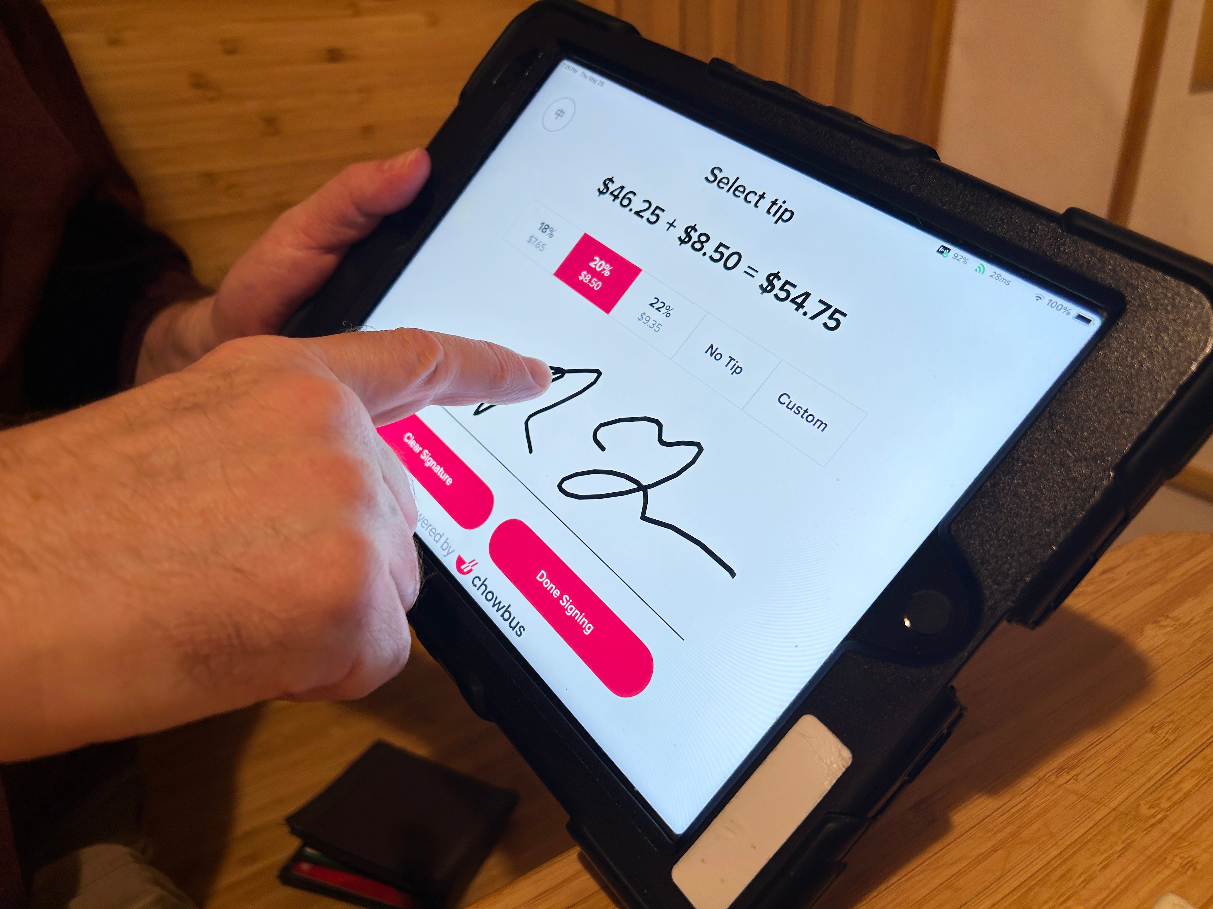 A customer uses their finger to sign their name on a credit card receipt presented on a tablet.