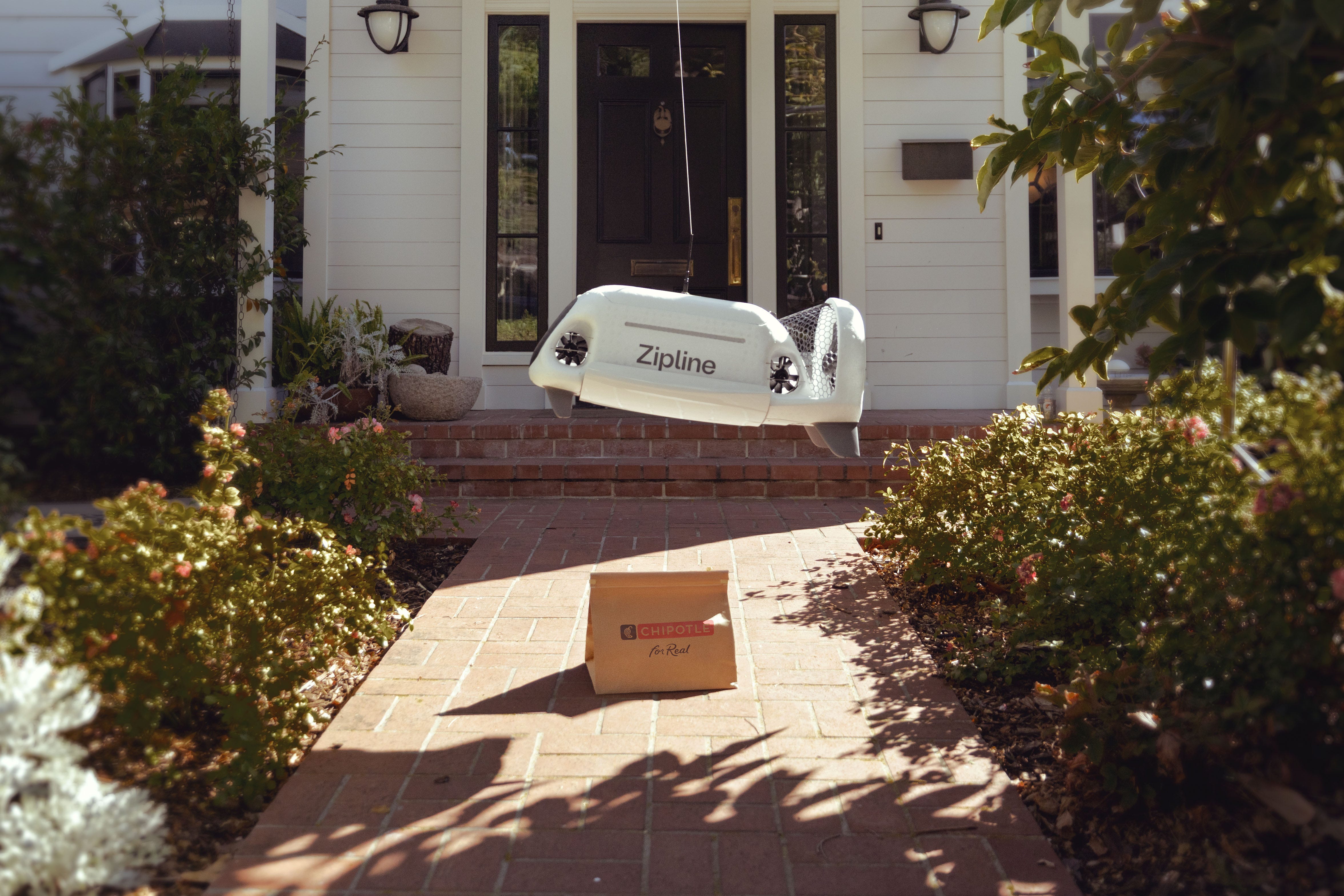 A Zipline drone delivers a Chipotle bag on a residential doorstep.