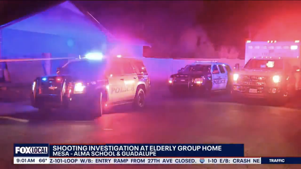 A police car and an ambulance with flashing lights at the scene of a shooting investigation.