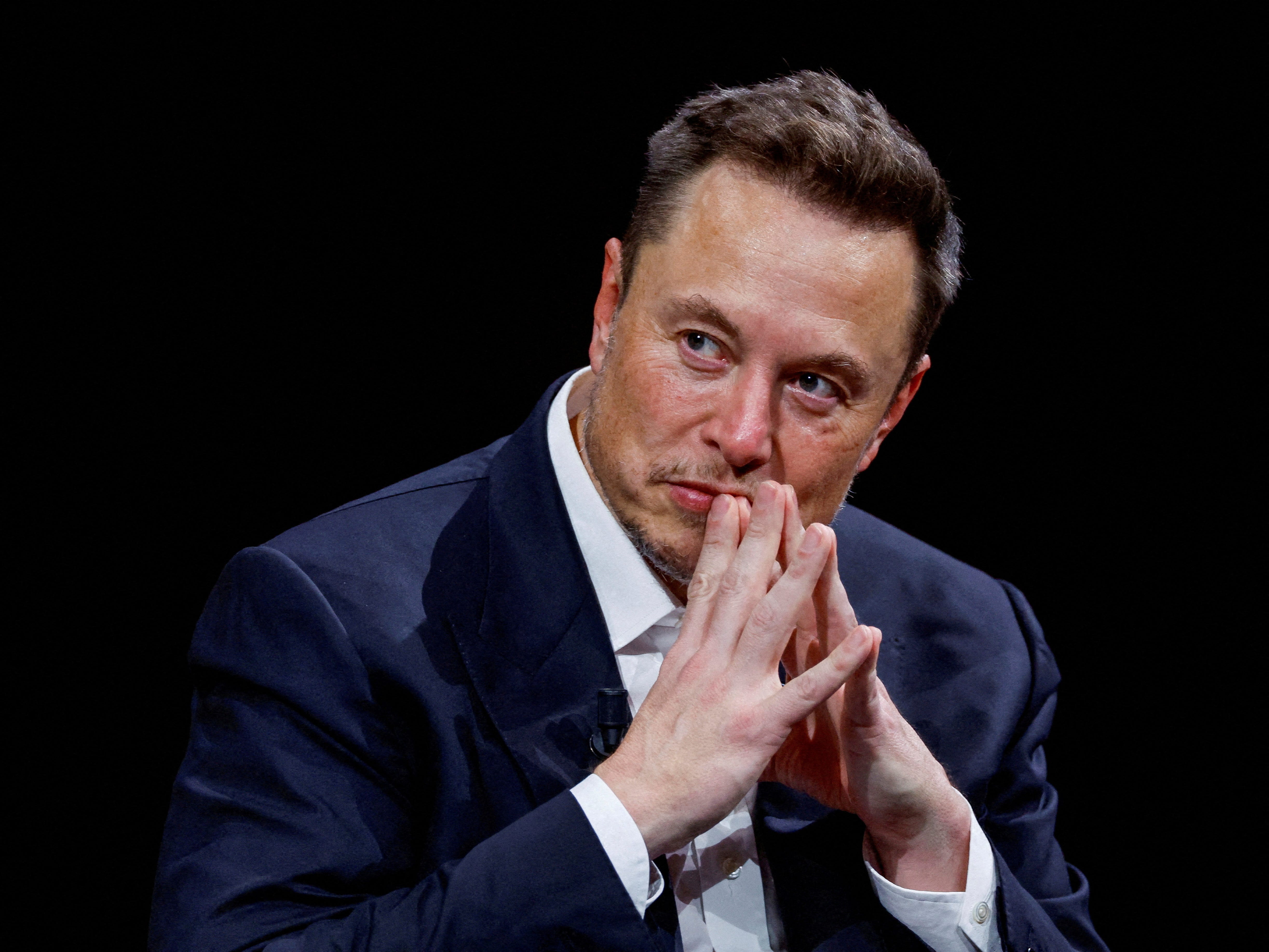 elon musk against black background making steeple gesture