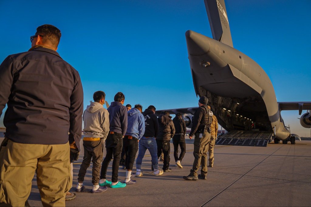 Deportees in restraints boarding a large cargo aircraft.
