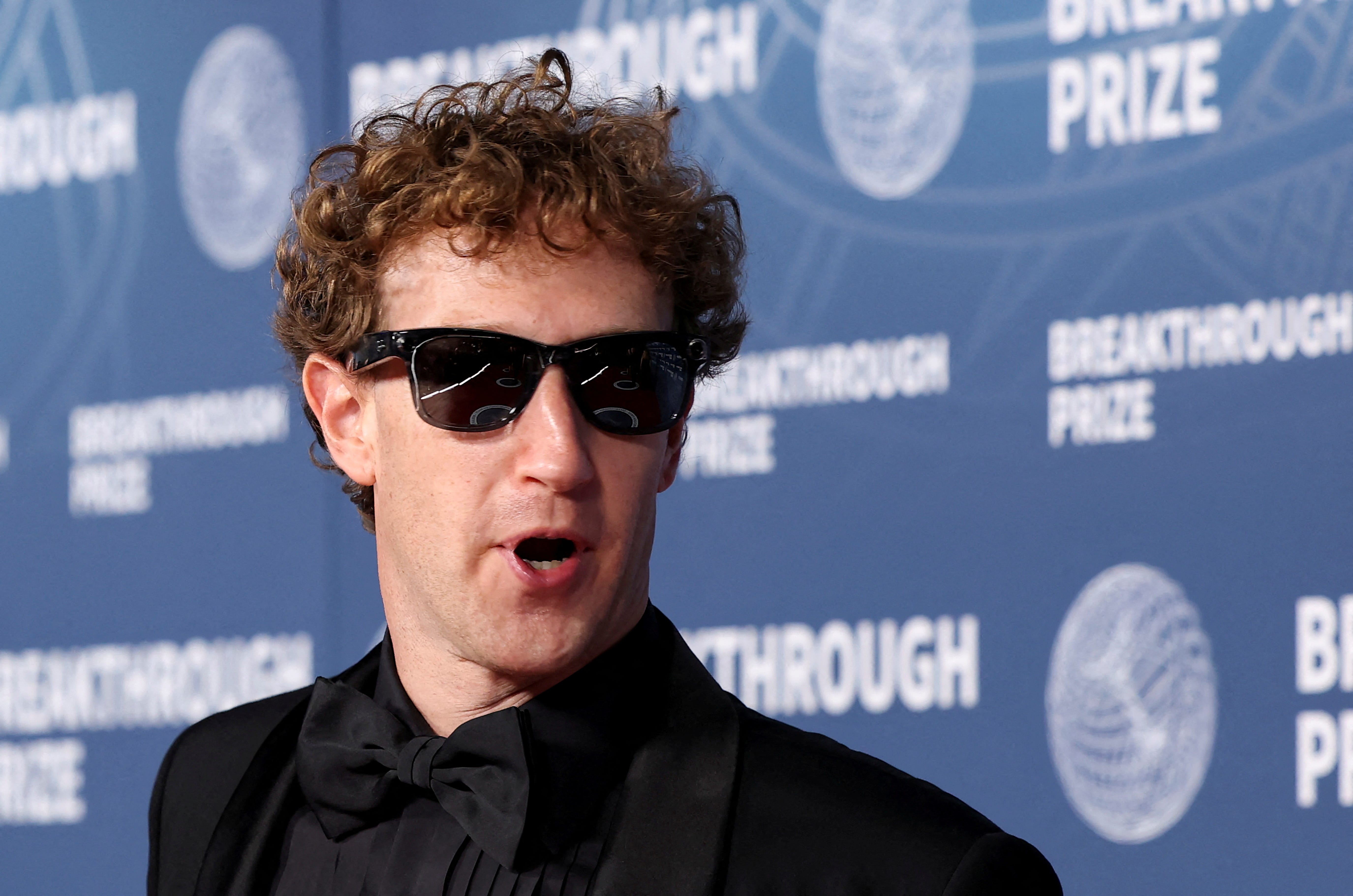 Mark Zuckerberg wearing sunglasses and a tux with a black shirt at an awards ceremony.