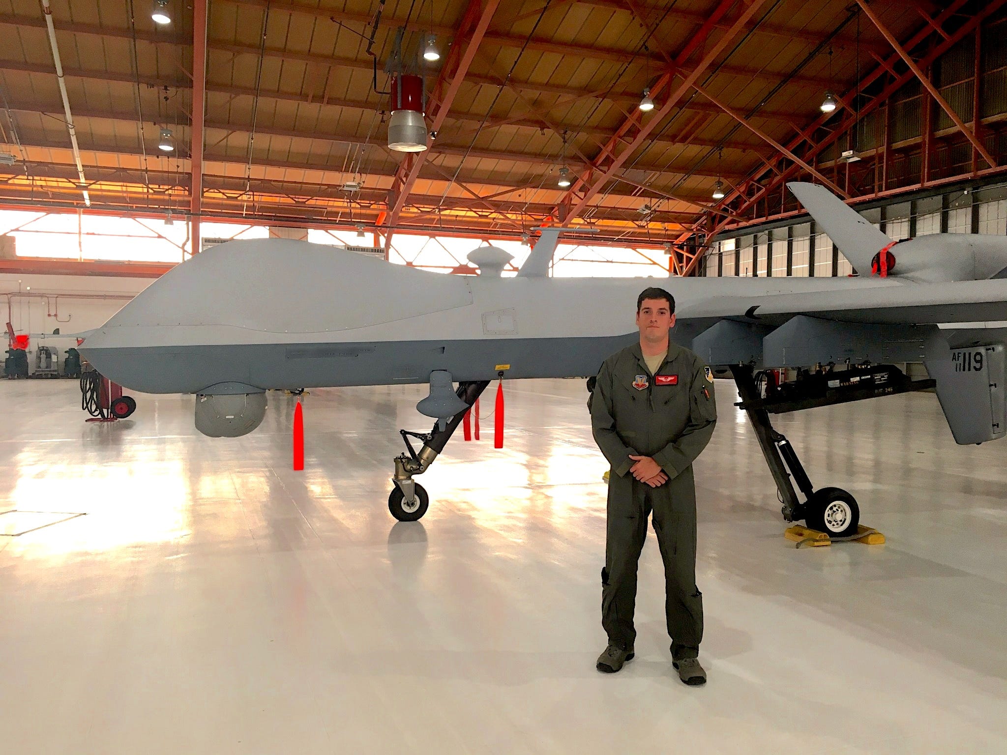 A man in military uniform standing in front of large drone.