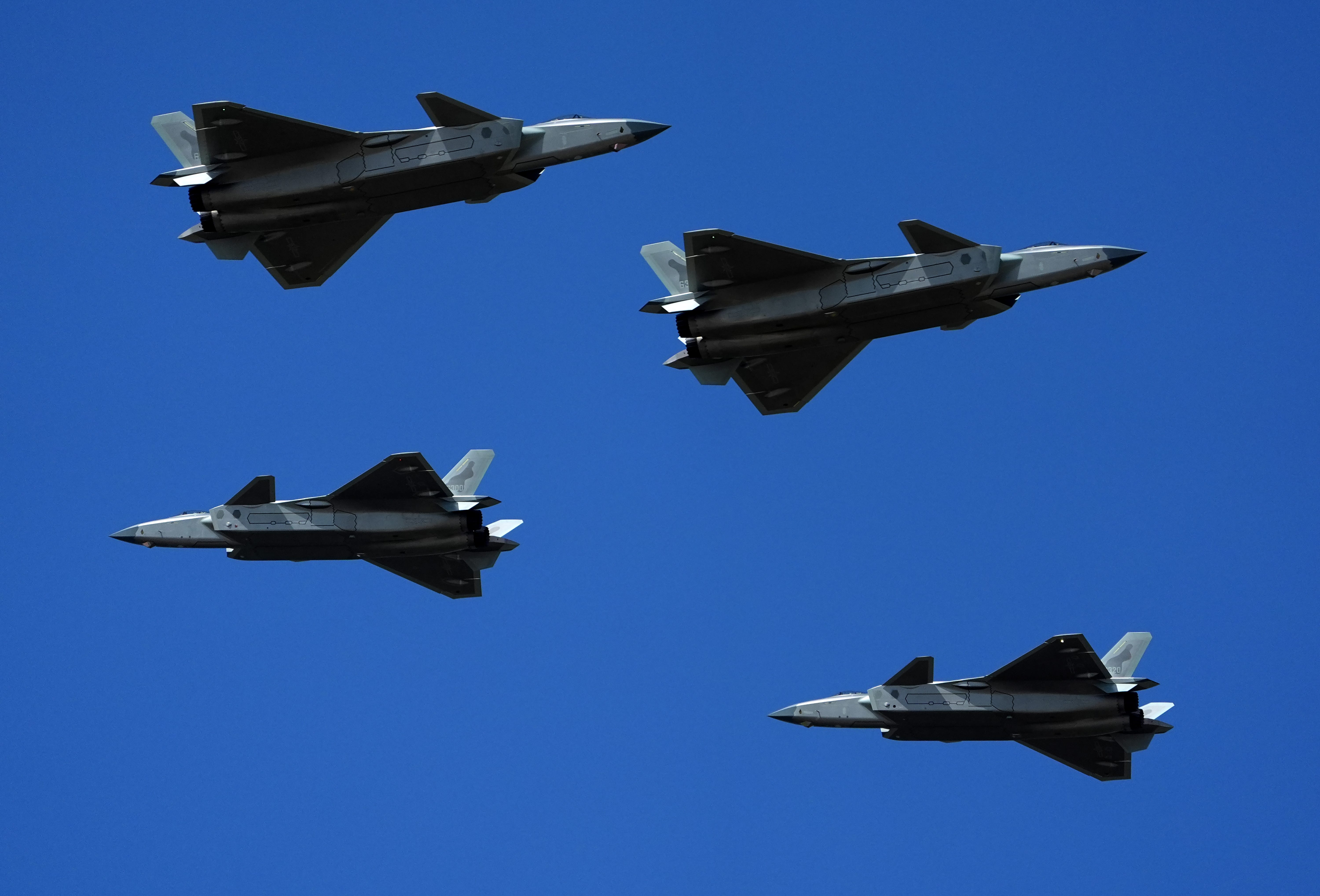 Four Chinese J-20 fighters fly in a blue sky.