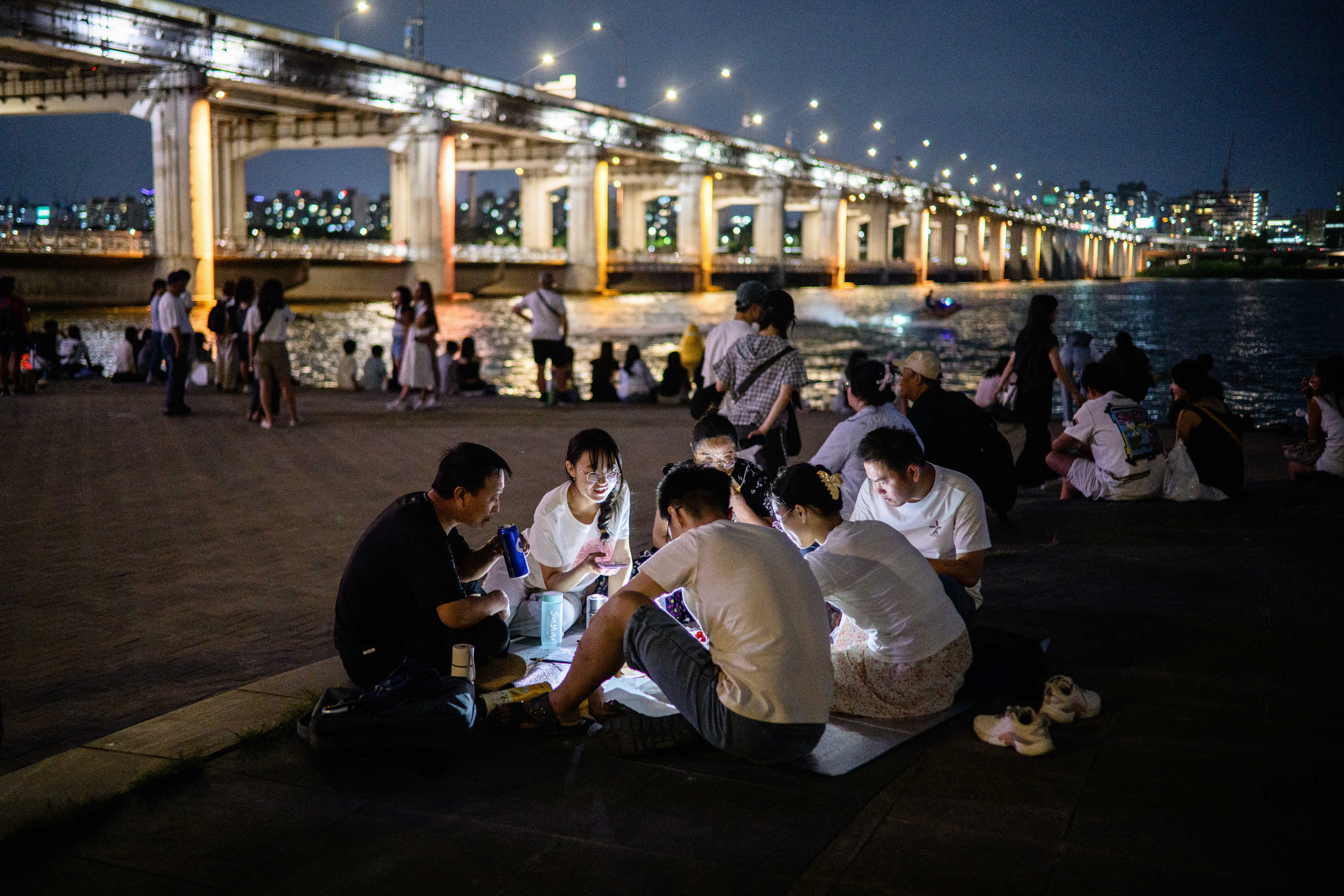 People gather for a picnic near the Banpo Bridge, which stretches over the Han River in Seoul on August 8, 2025.