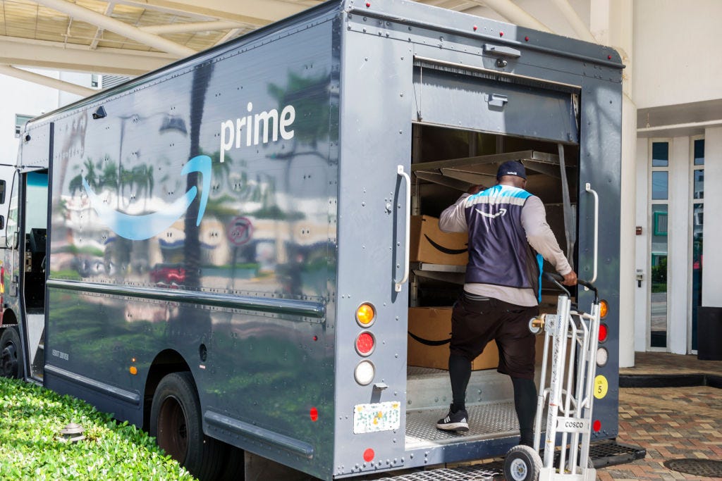 An Amazon worker getting packages out of a truck that has an Amazon logo.