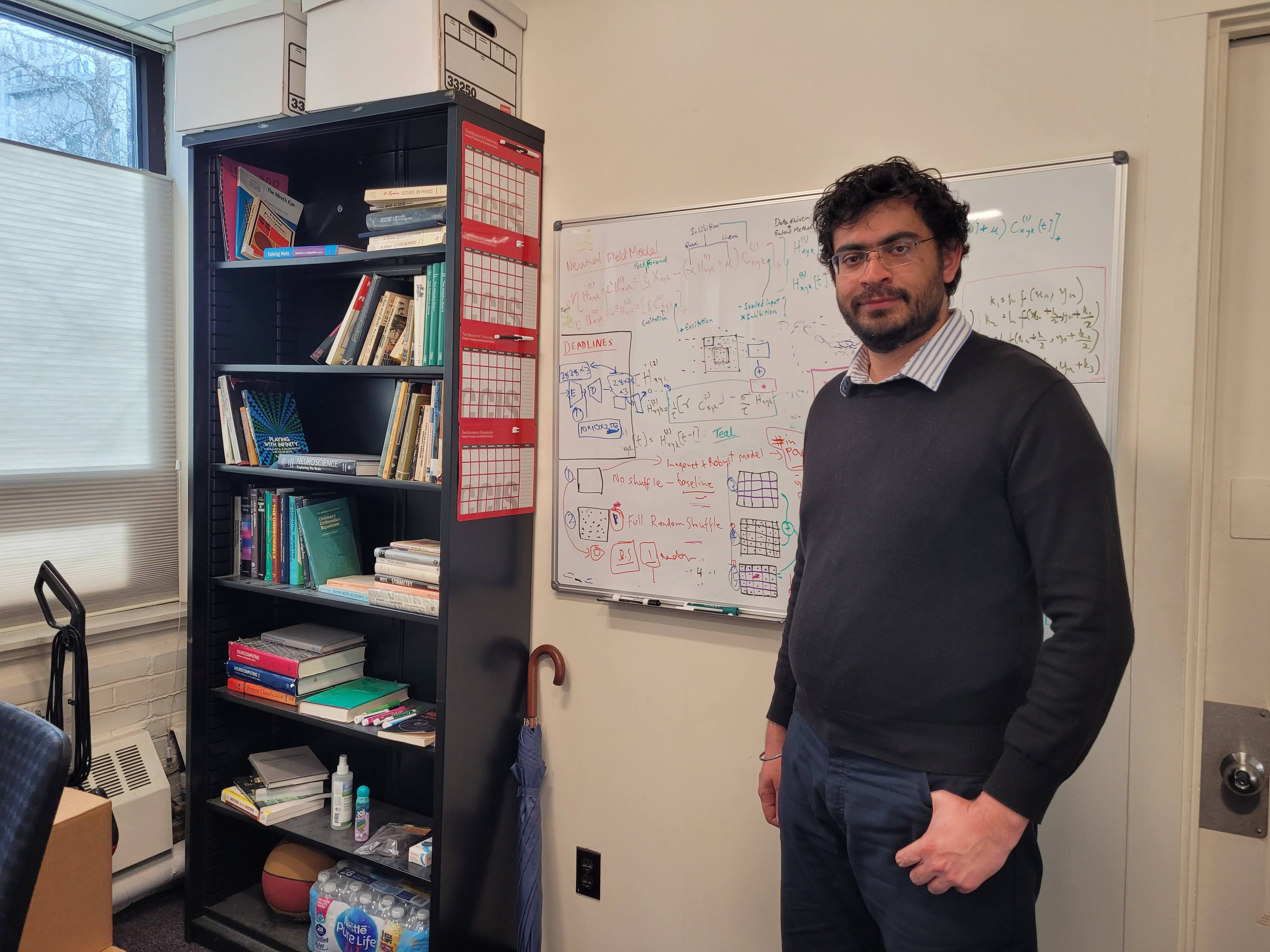 Girik Malik is standing in front of a whiteboard in his office.