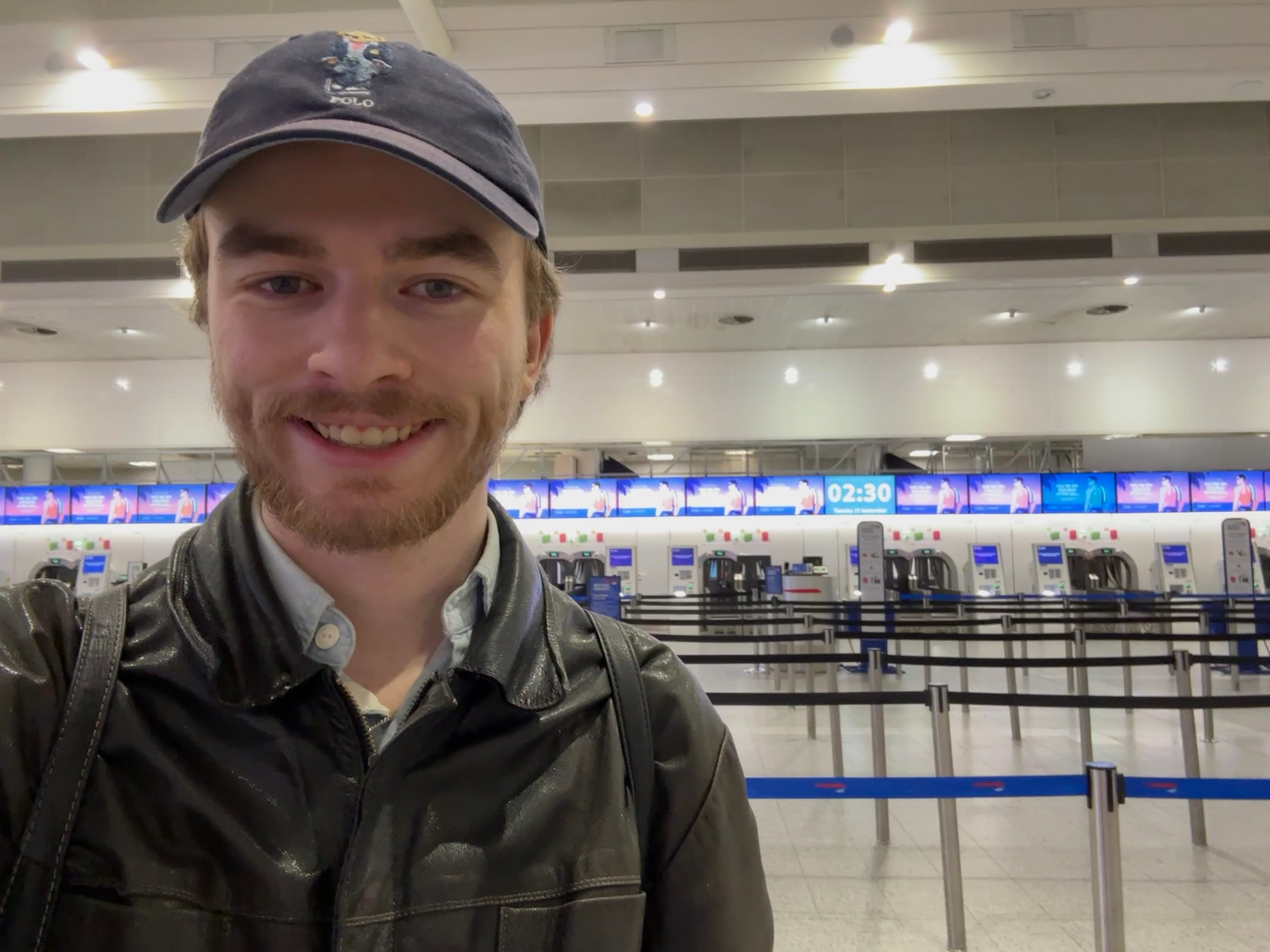 The author takes a selfie in front of an empty check-in area at London Gatwick Airport where a clock shows the time is 2:30 a.m.