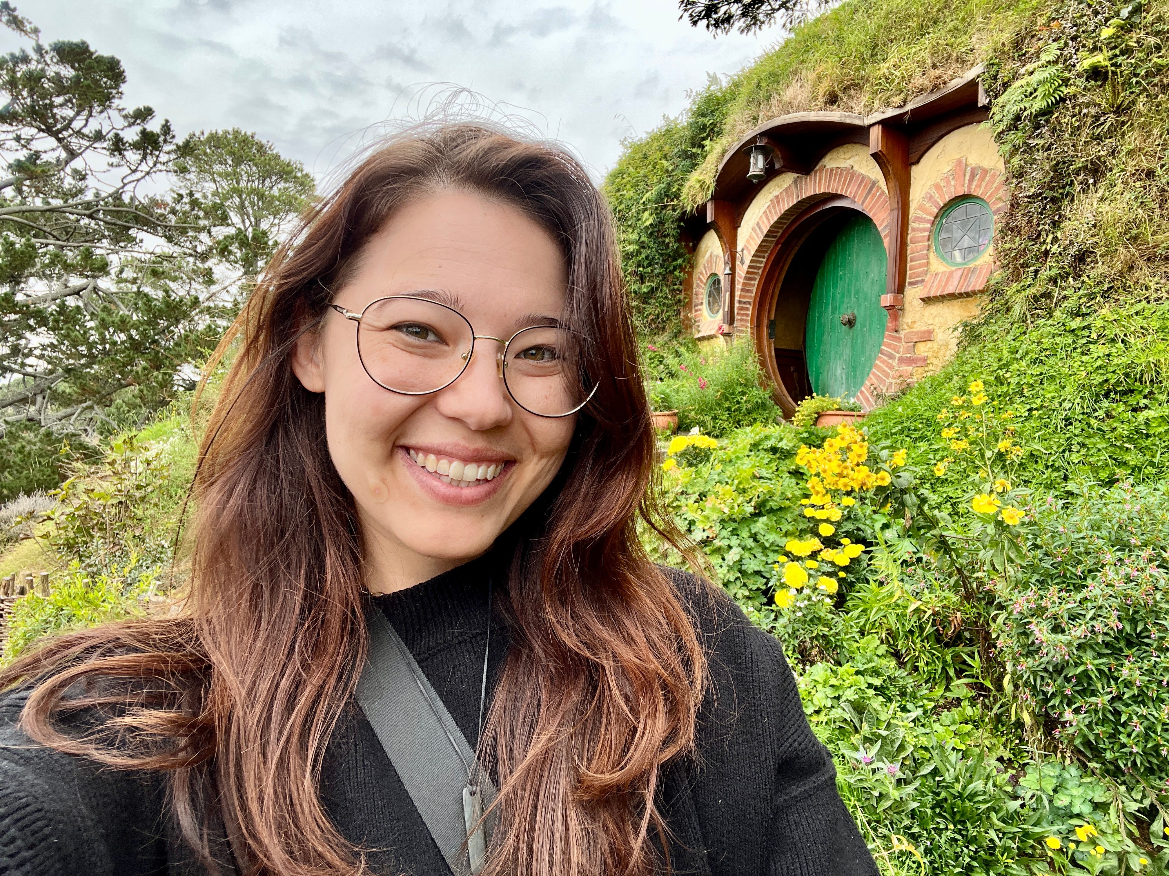 Author Ashley Probst smiling in front of hobbit house in New Zealand