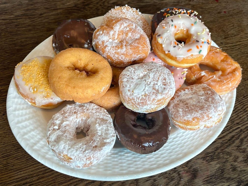 16 doughnuts on a white oval plate sitting on a wood table.