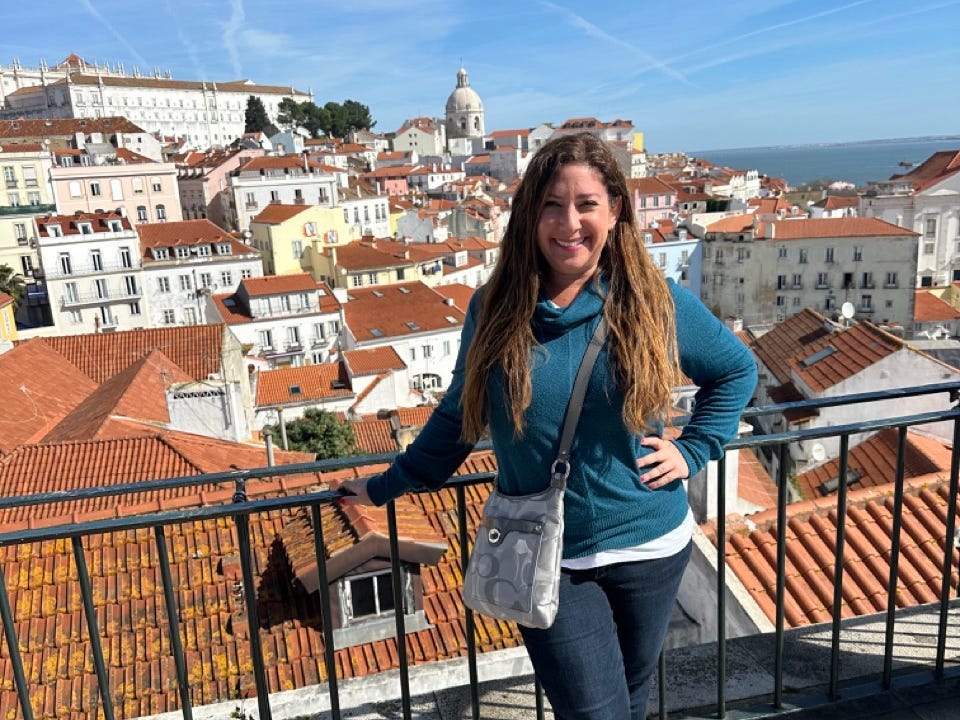 Author Jill SChildhouse posing on railing in Lisbon with aerial view of city behind her