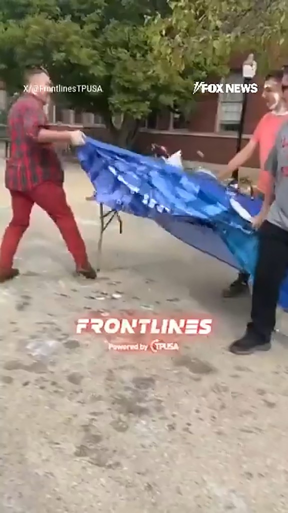Man in a red plaid shirt and red pants flips over a table covered with a blue tarp.