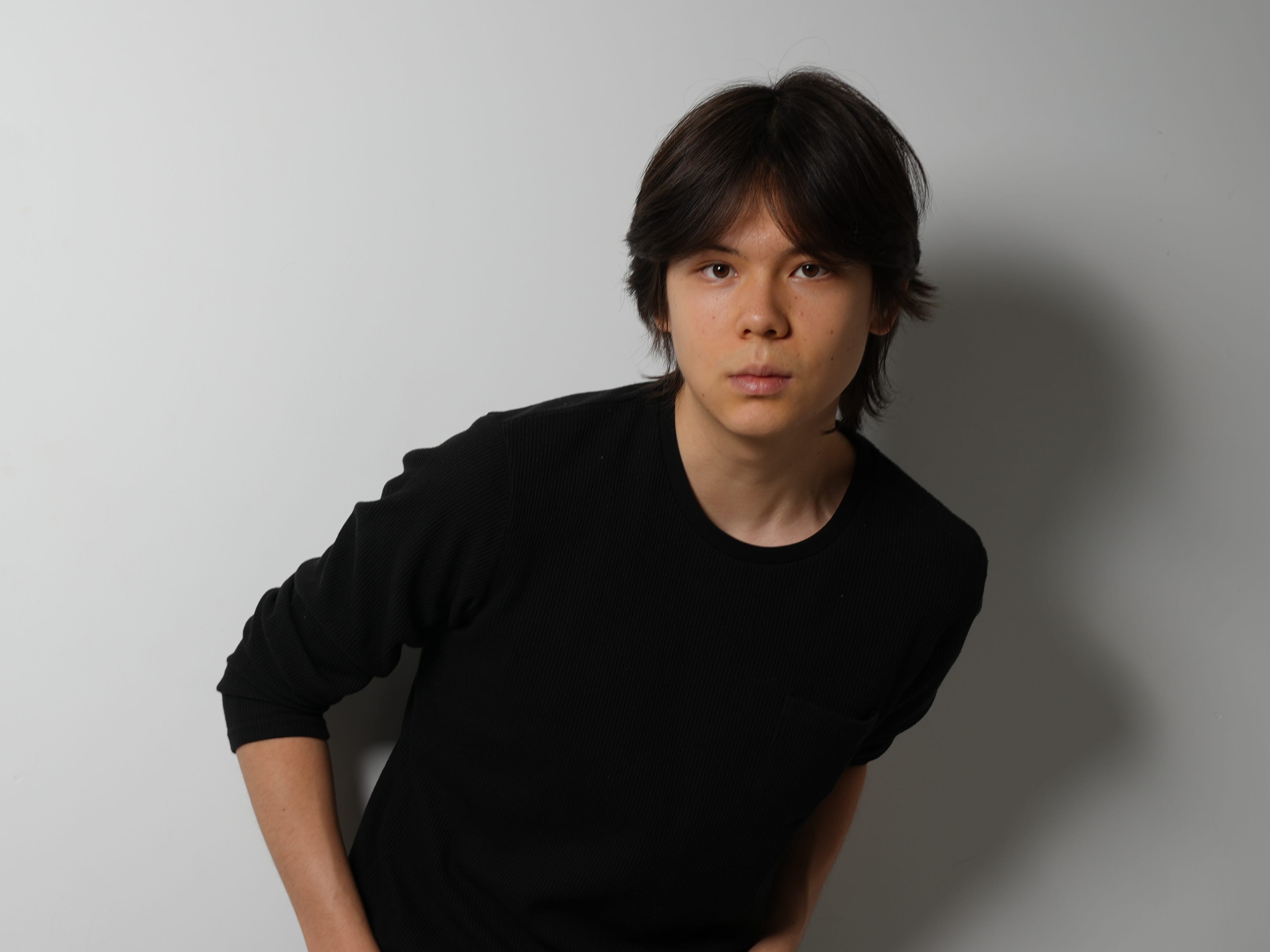 Arlan Rakhmetzhanov, standing in front of a white background, wearing a black shirt and jeans, with his hands in his pockets.