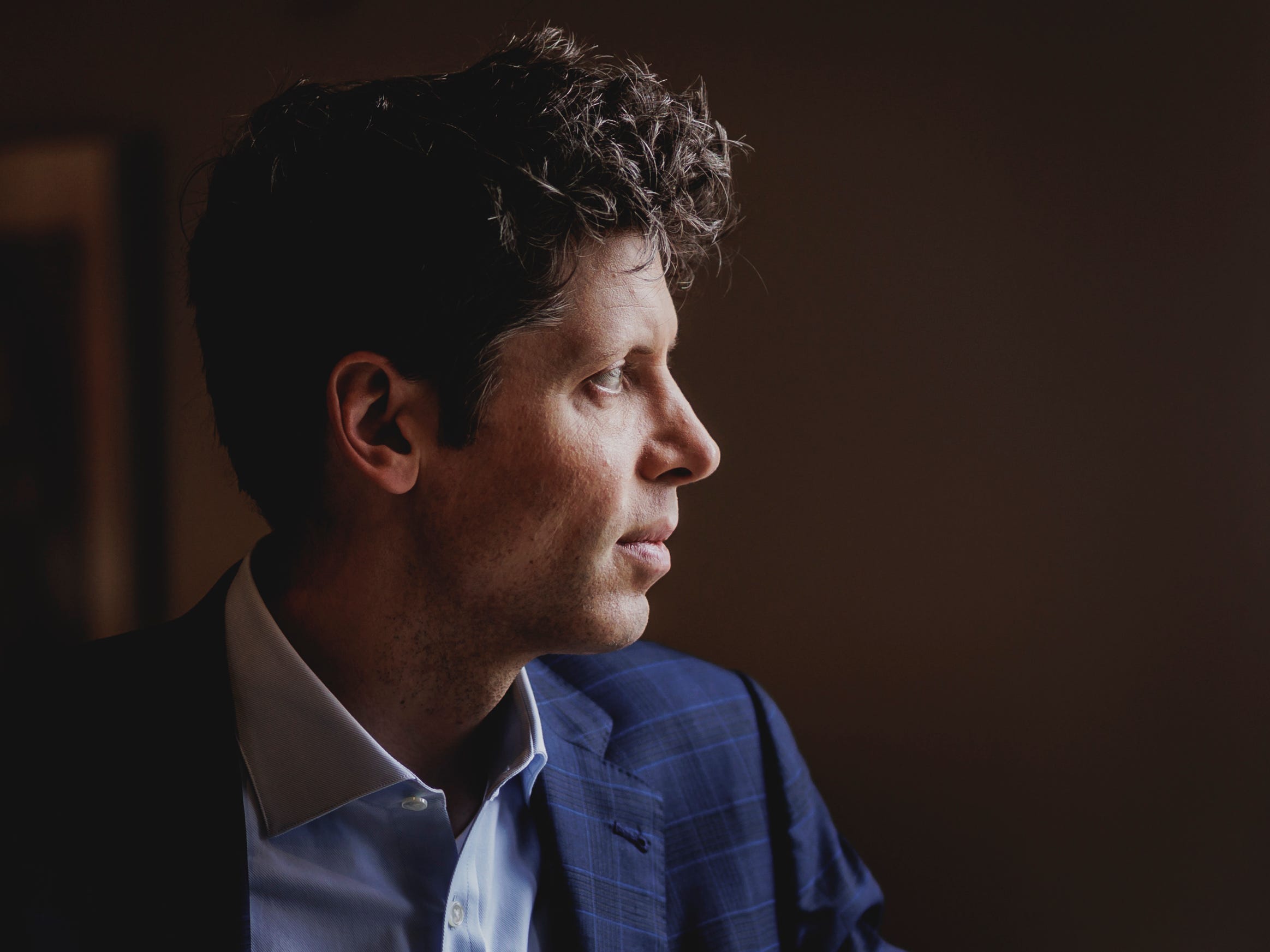 Sam Altman's profile, standing in front of a window.