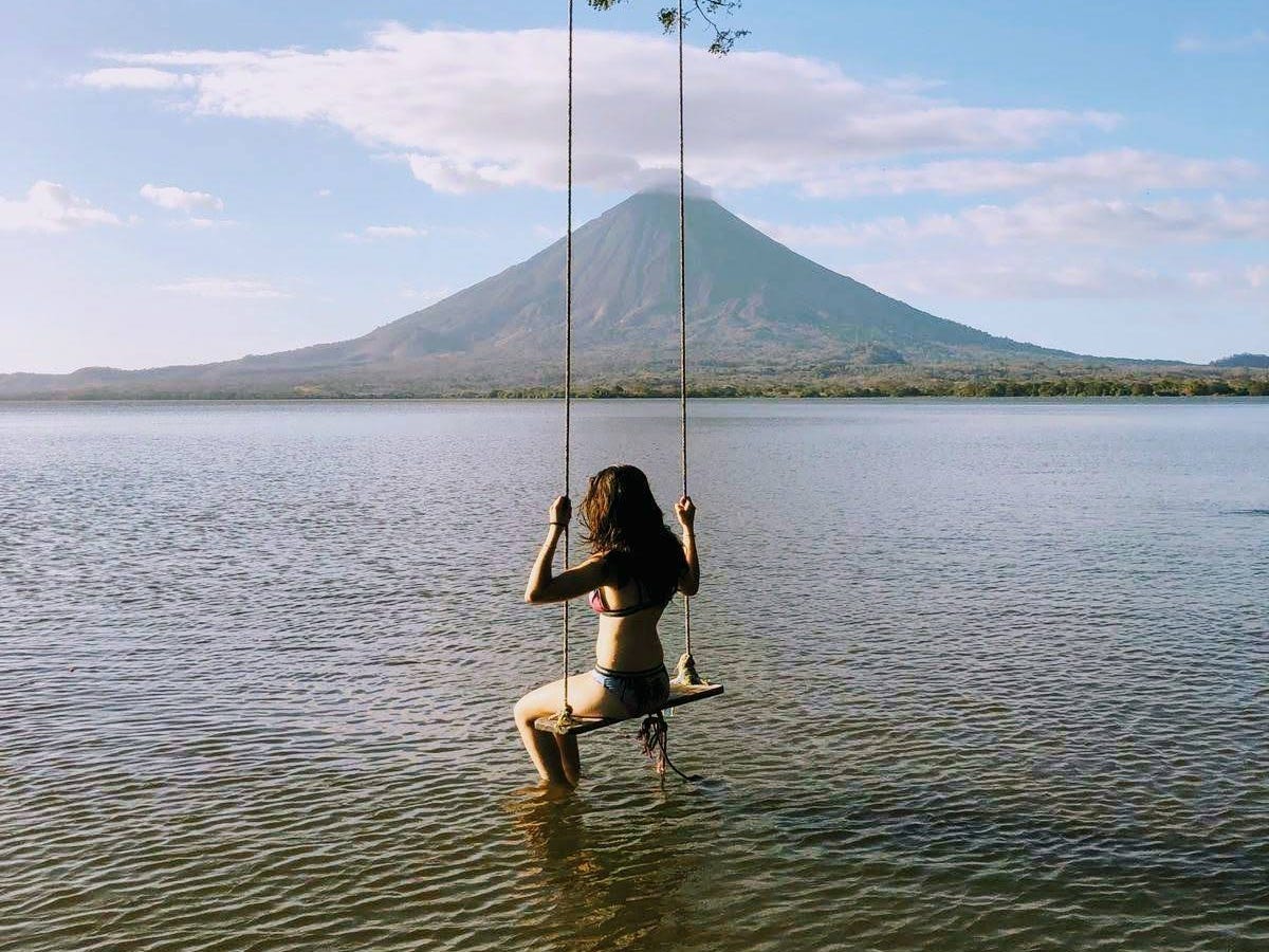 Cait Charles swinging above water with a mountian in the background.