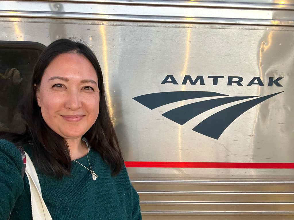 Malia stands in front of the Amtrak logo on a train.