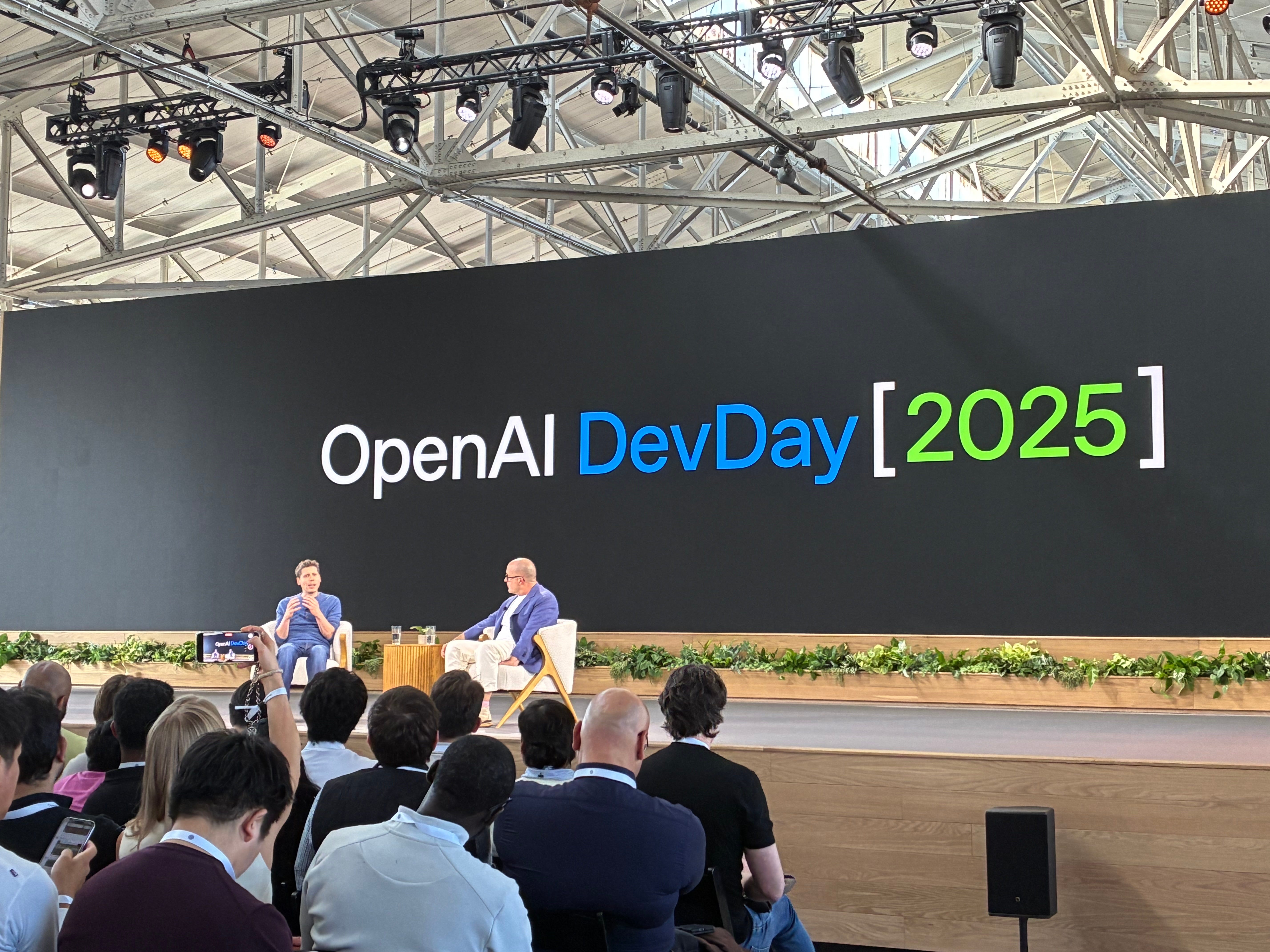 Sam Altman (left) and Jony Ive (right) chat on stake at OpenAI's DevDay conference