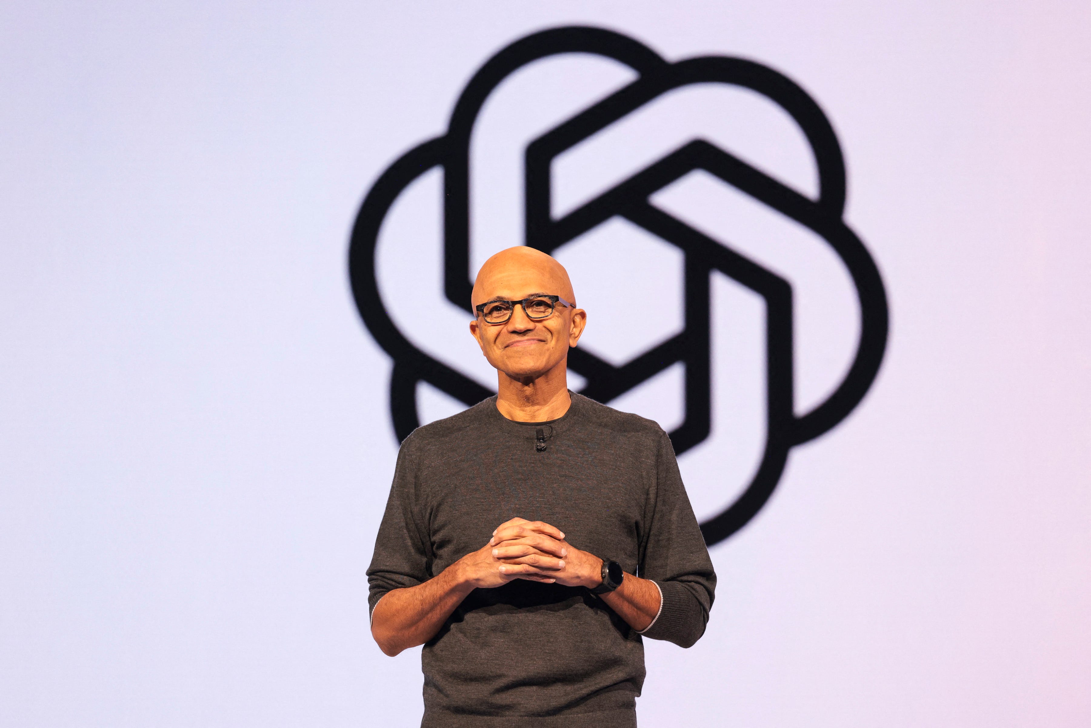 Satya Nadella is speaking in front of an OpenAI logo.