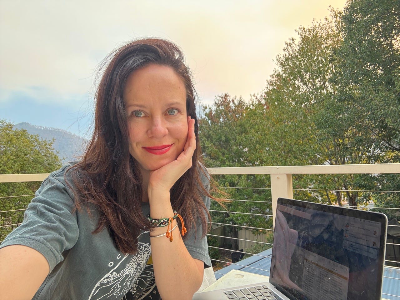 Author Melissa Noble smiling on a deck in front of her laptop