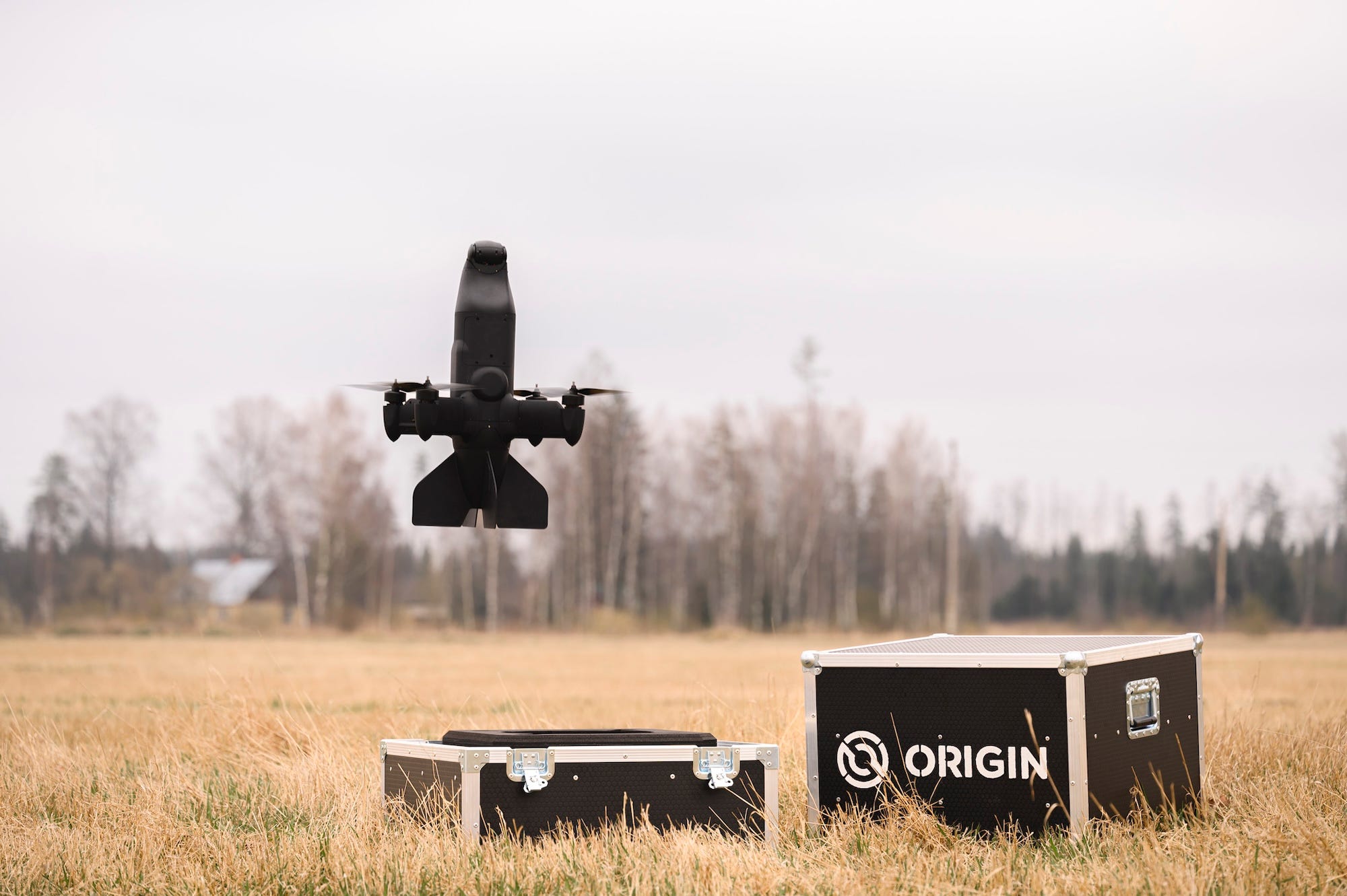 A black piece of weaponry hovers in the sky above a straw-colored grassy ground and two black boxes, one of which has 'Origin' written on it