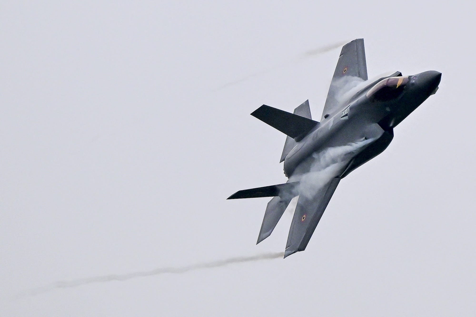a grey fighter jet leaning to one side against a grey sky