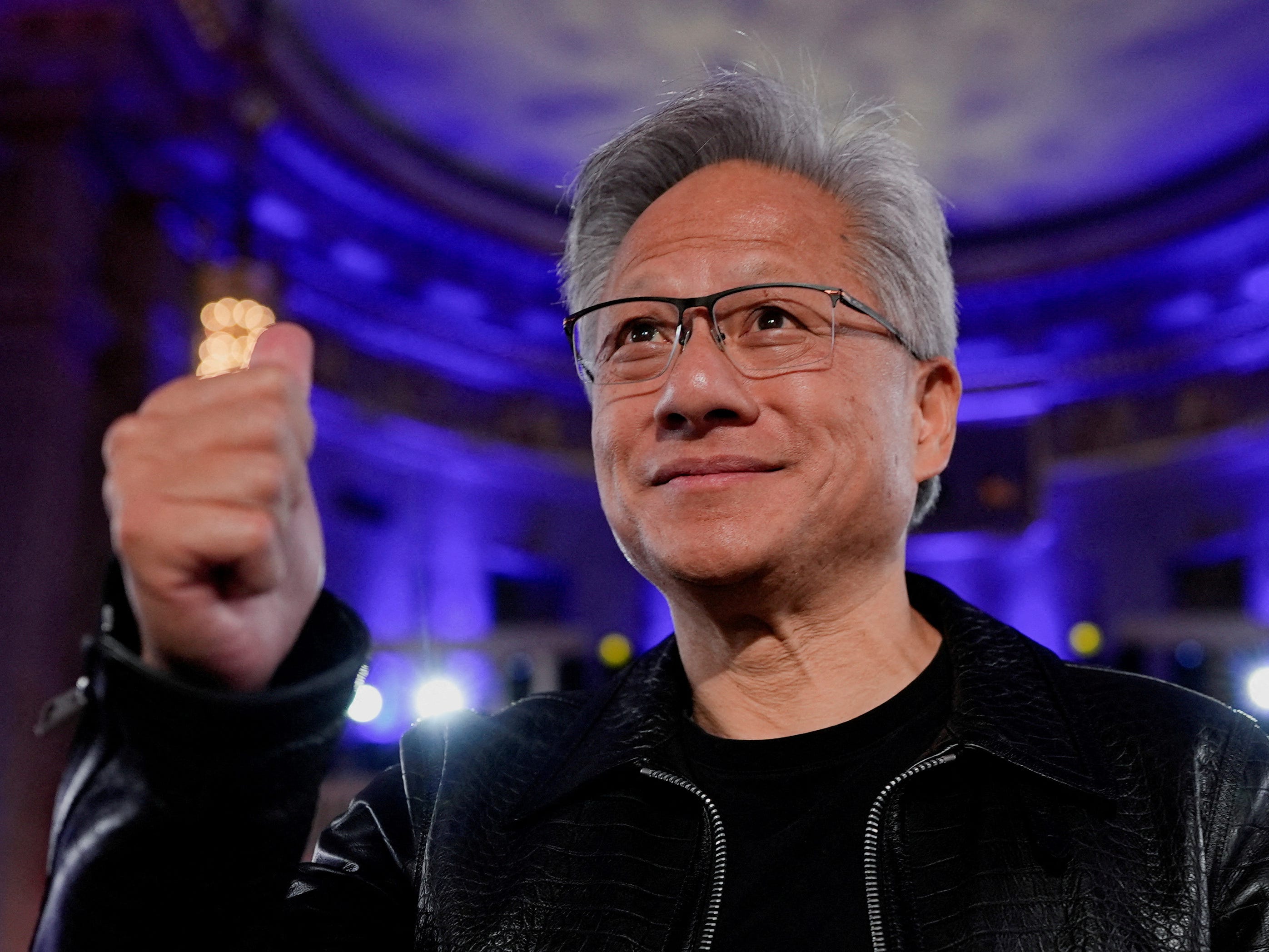 Jensen Huang gives a thumbs up in a blue-lit room.