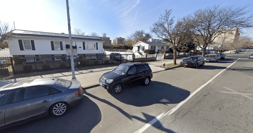 Street view of 1405 Louis Nine Boulevard, a white house with solar panels on the roof, a black fence, and a car in front.