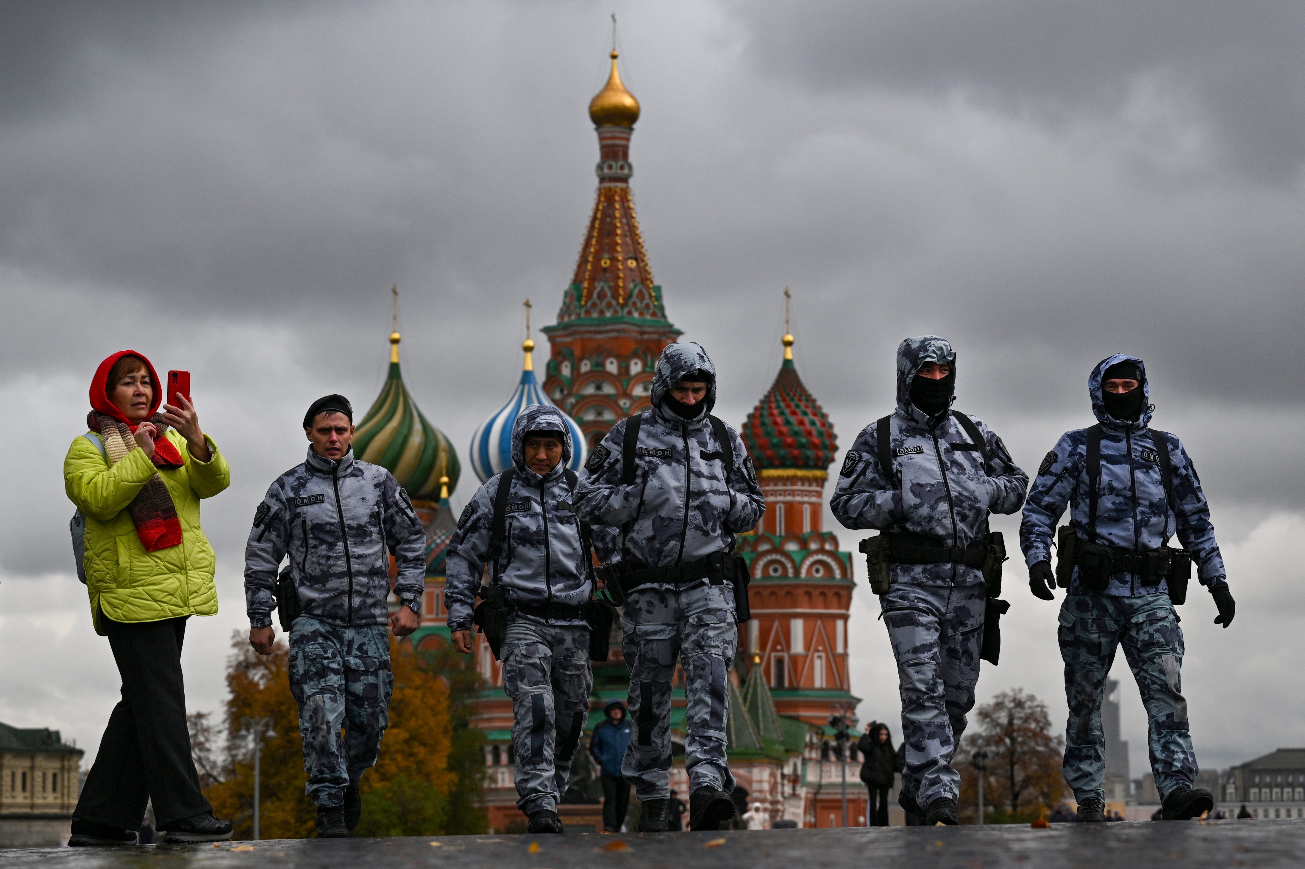 A woman uses her smartphone as riot policemen walk along Red Square in front of St. Basil's Cathedral on an autumn day in central Moscow