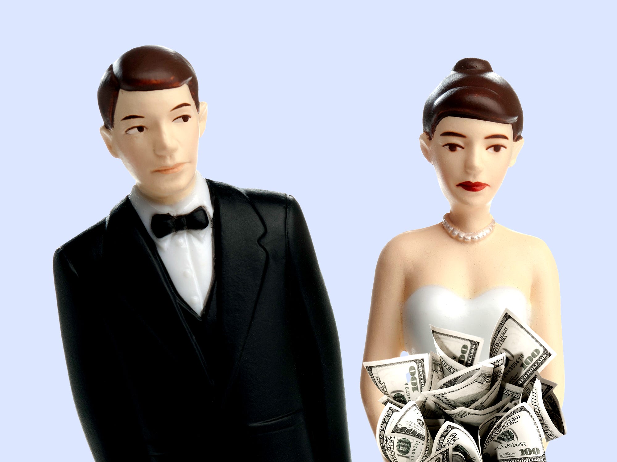 A male cake topper leaning away from a female cake topper holding a bouquet of money.