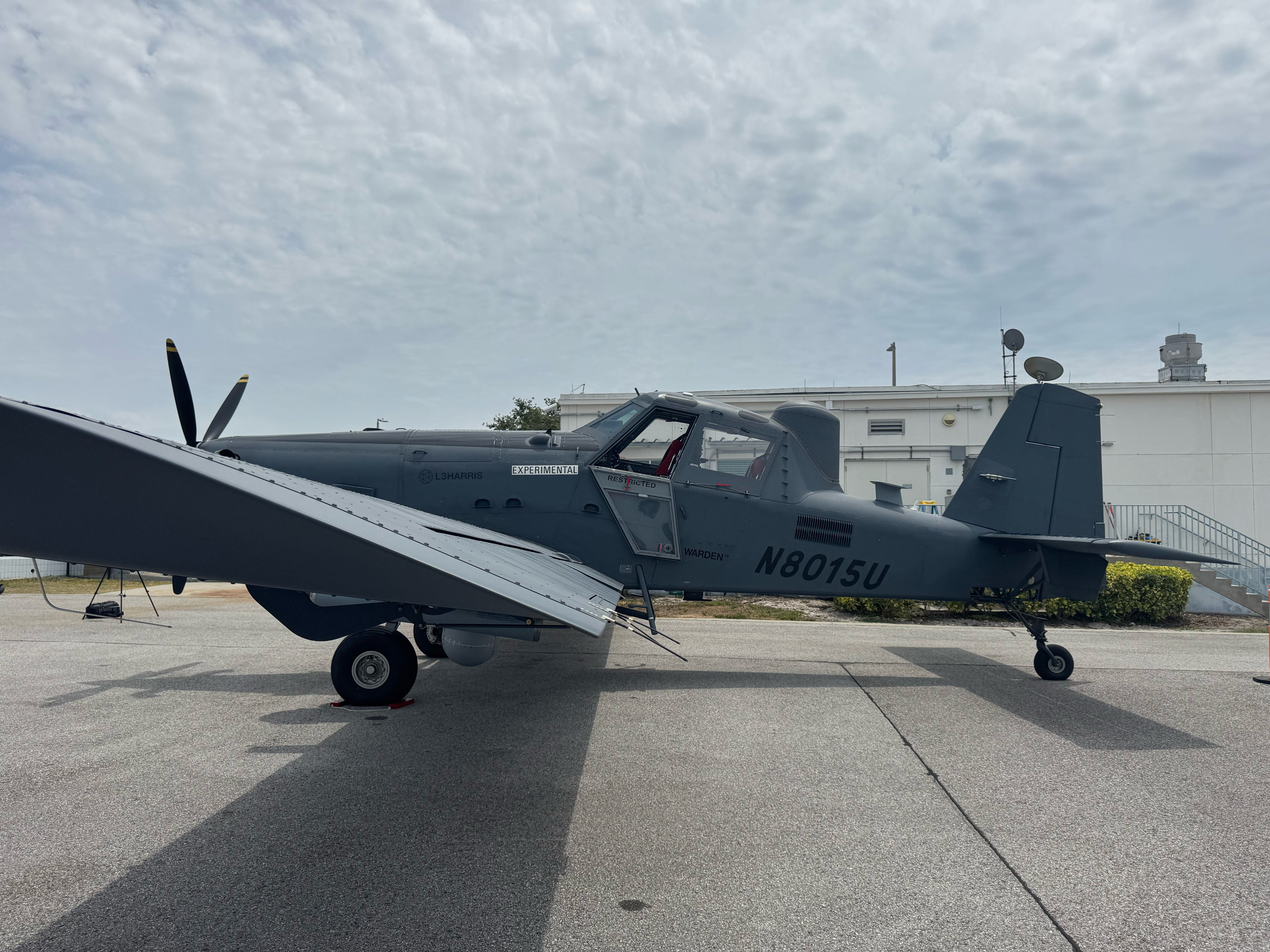 The side of L3Harris' Sky Warden is seen sitting on an airfield with a grey overcast sky in the background.