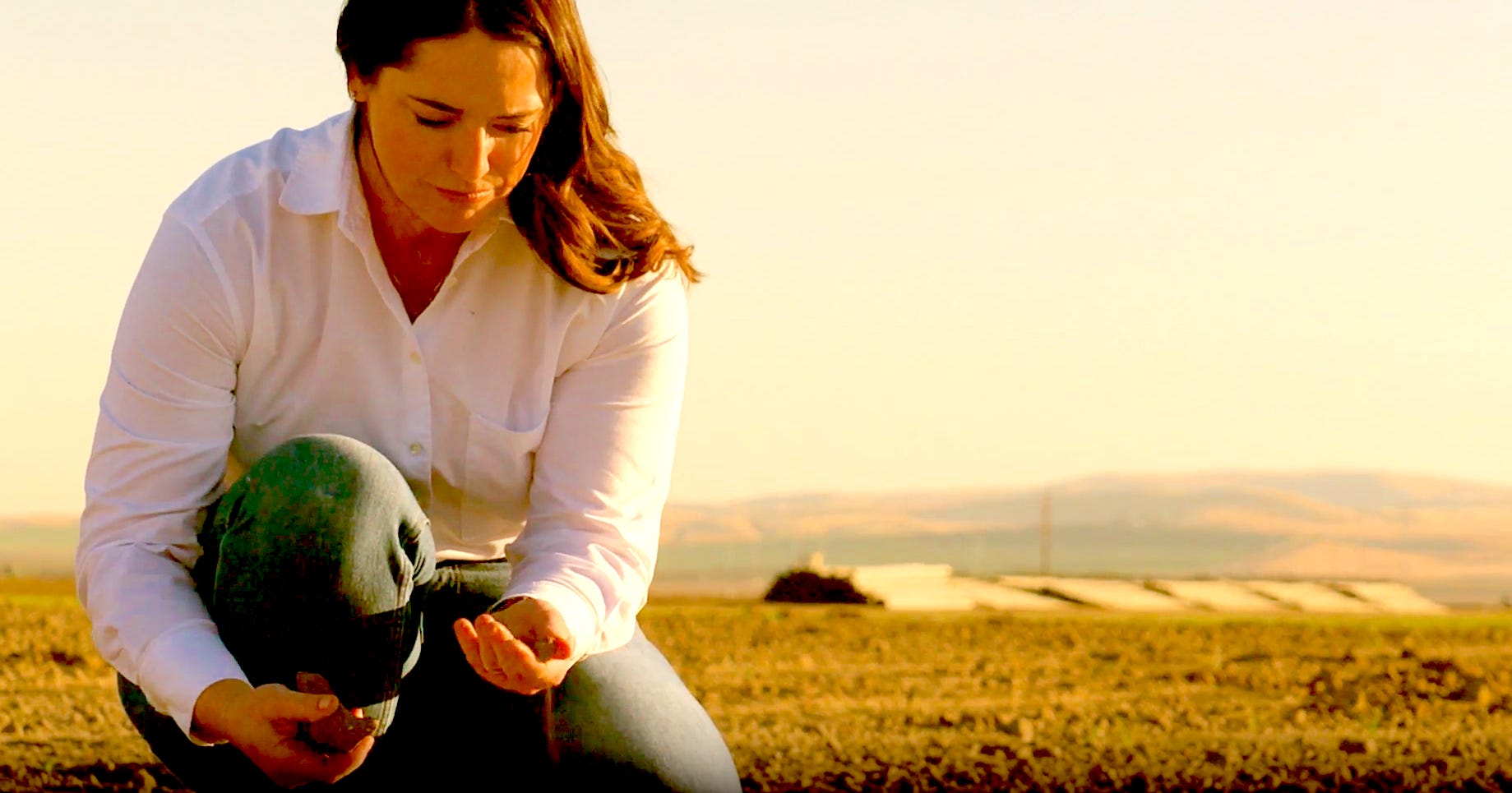 woman bent down to ground picking up soil in her hands