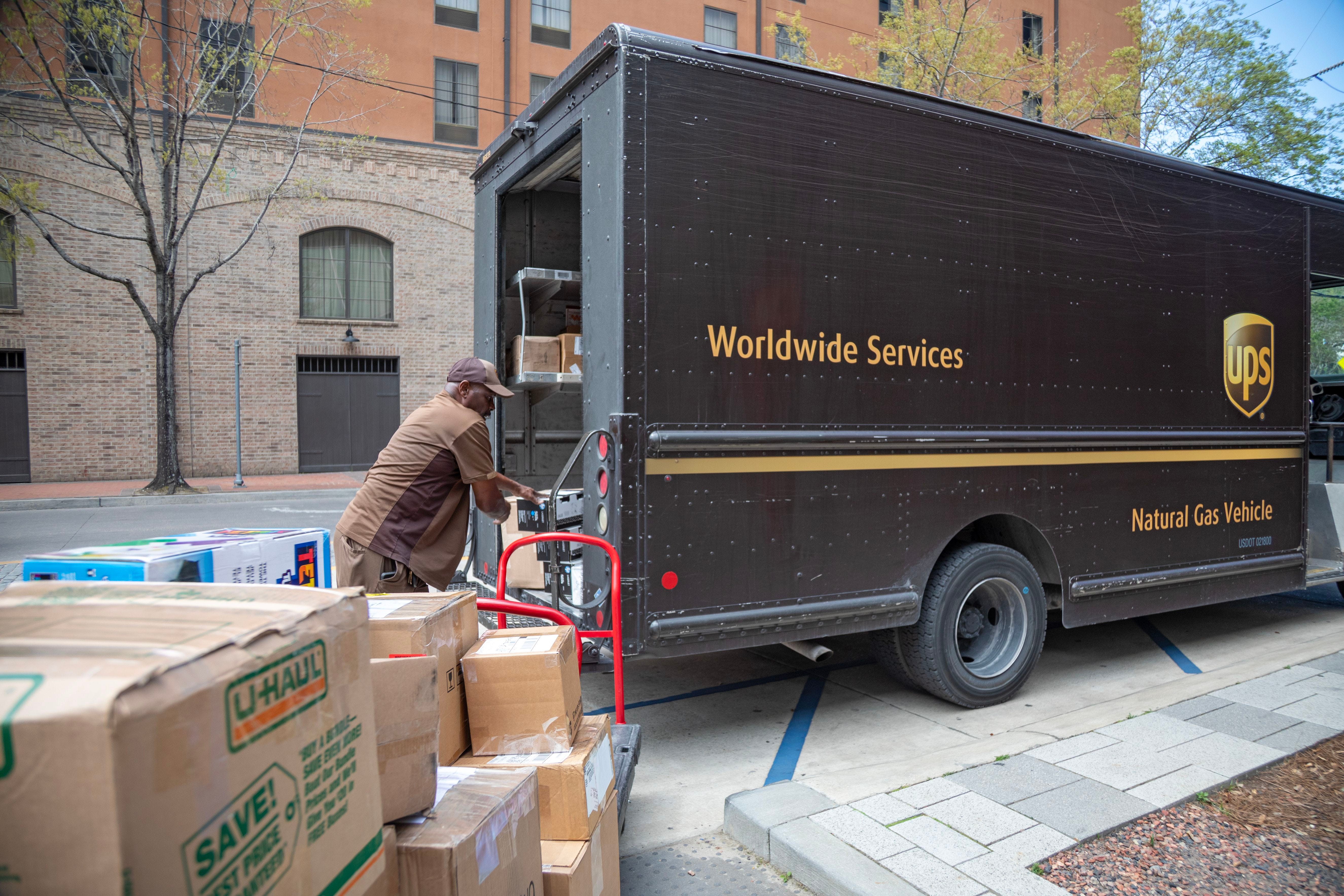 A UPS worker handles boxes at the back of a brown UPS truck on a street.