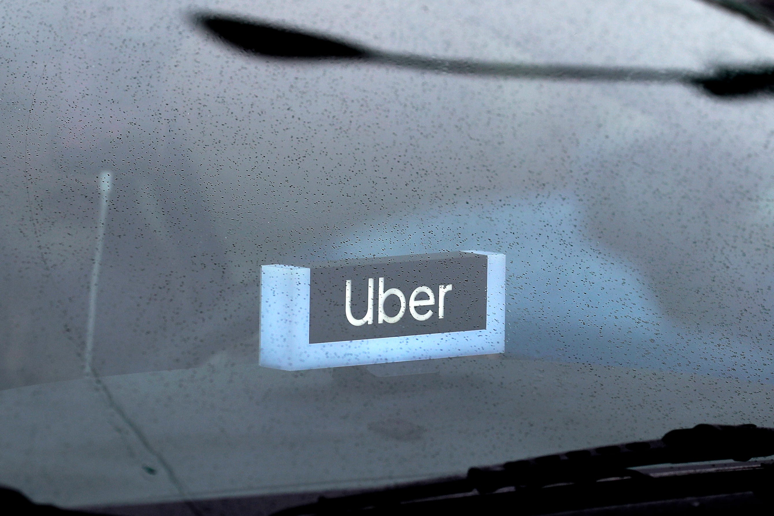 An Uber light sits on the dash of a car behidn a windshield.