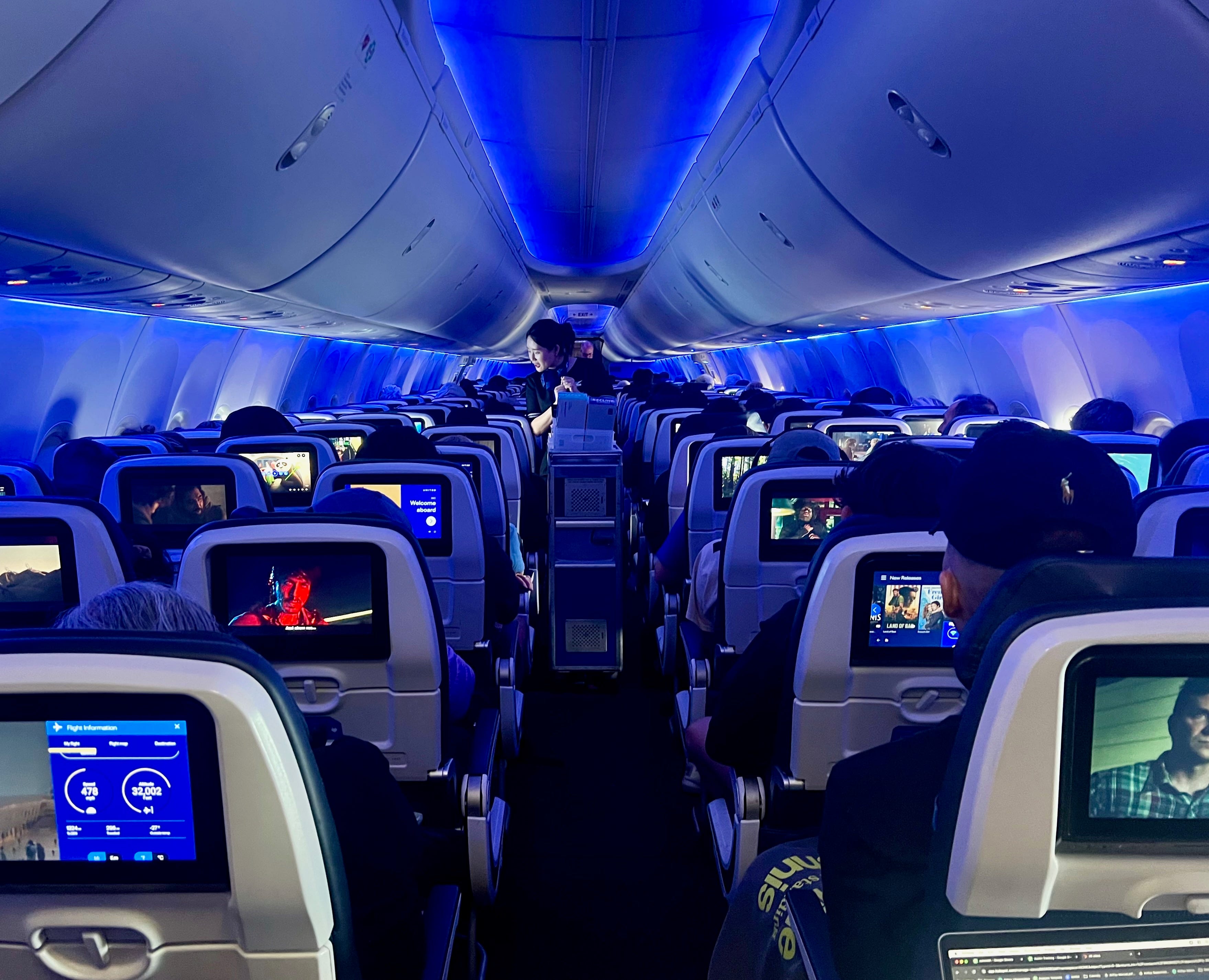 The United Next cabin with a flight attendant in the aisle serving drinks.