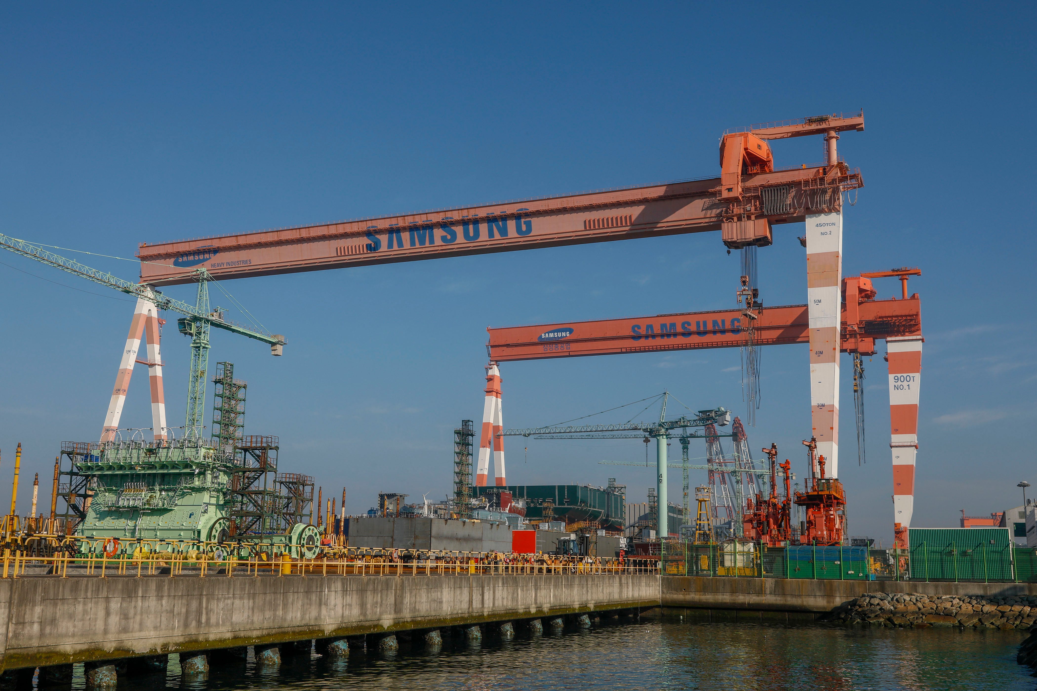 A South Korean shipyard with large cranes and structures and a clear blue sky in the background.