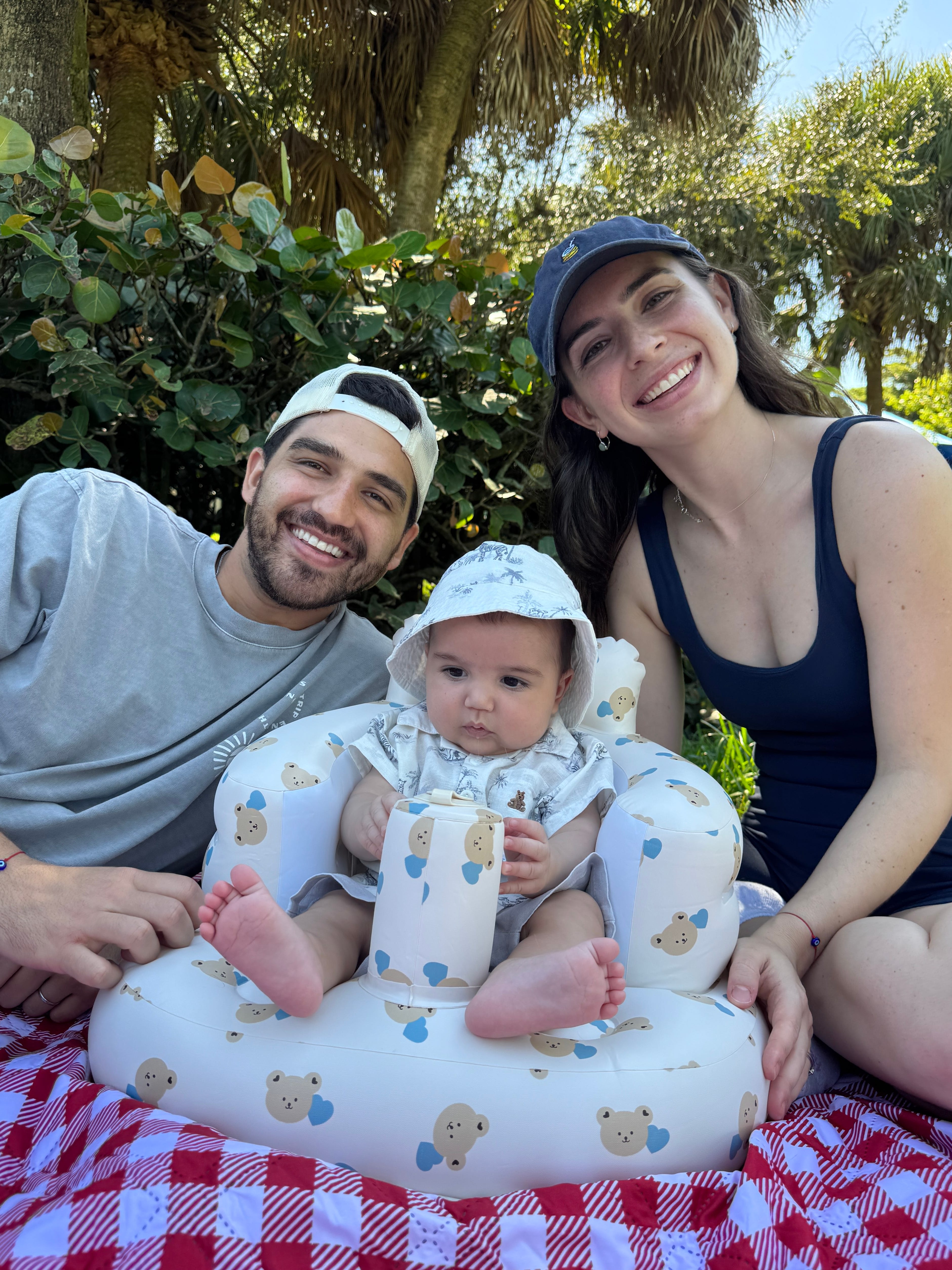 A man, a woman, and a baby smile as they lay on a blanket