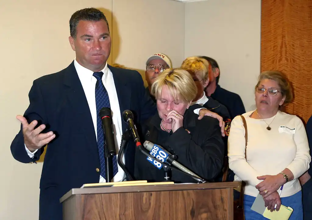 NYFD Battalion Chief James J. Riches and his wife Rita Riches speaking at a press conference with others behind them.
