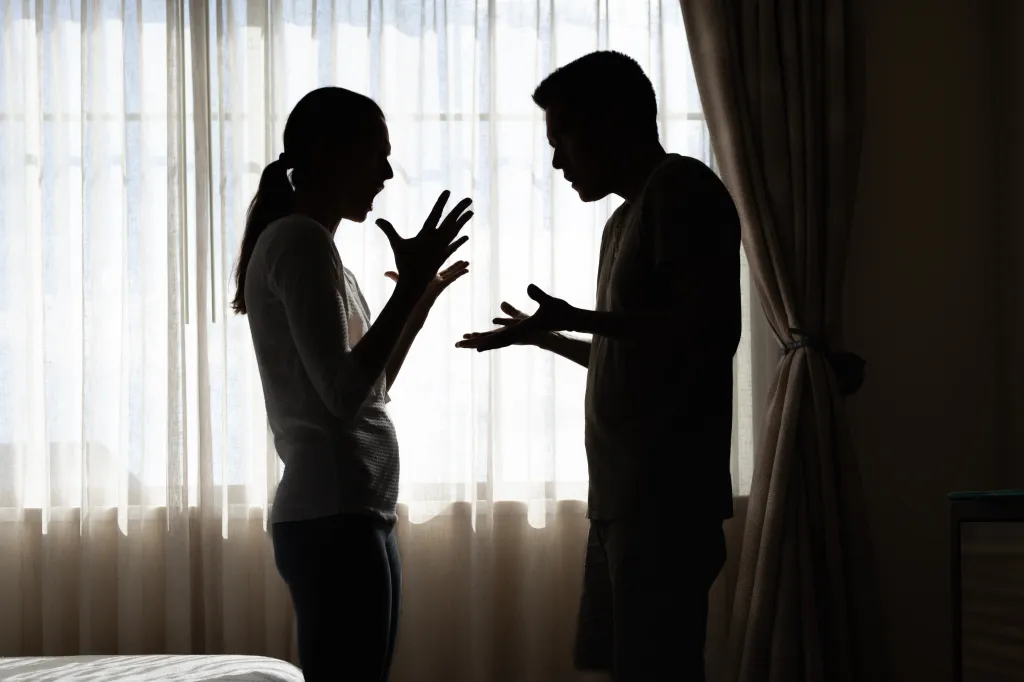 Silhouette of a couple arguing, with the woman gesturing angrily and the man looking down.