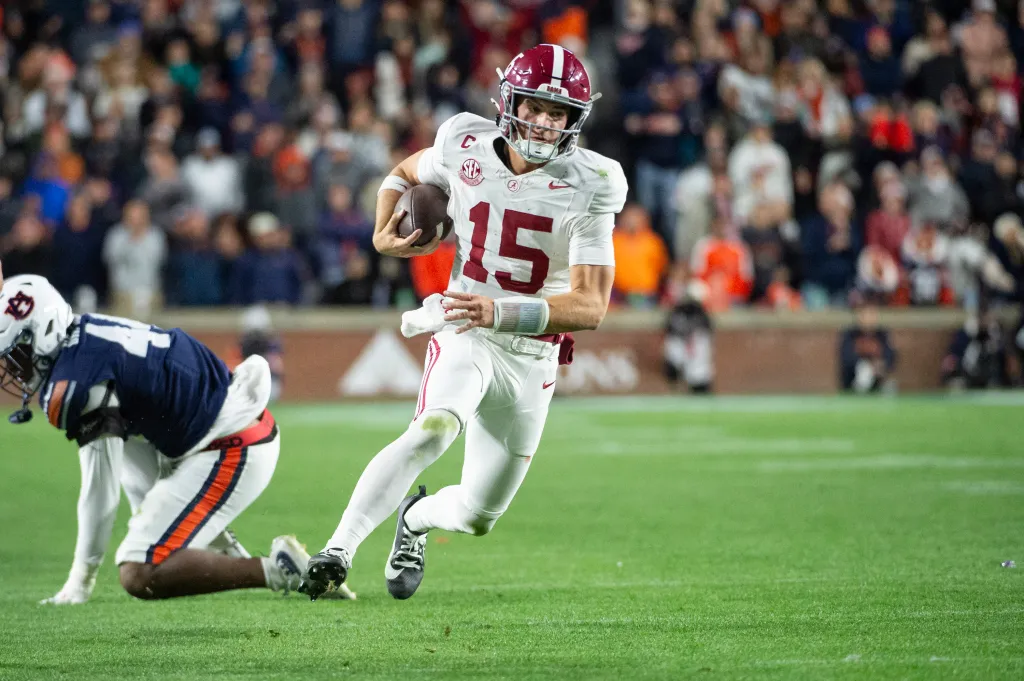 Alabama quarterback Ty Simpson running the ball past Auburn defensive lineman Darrion Smith.