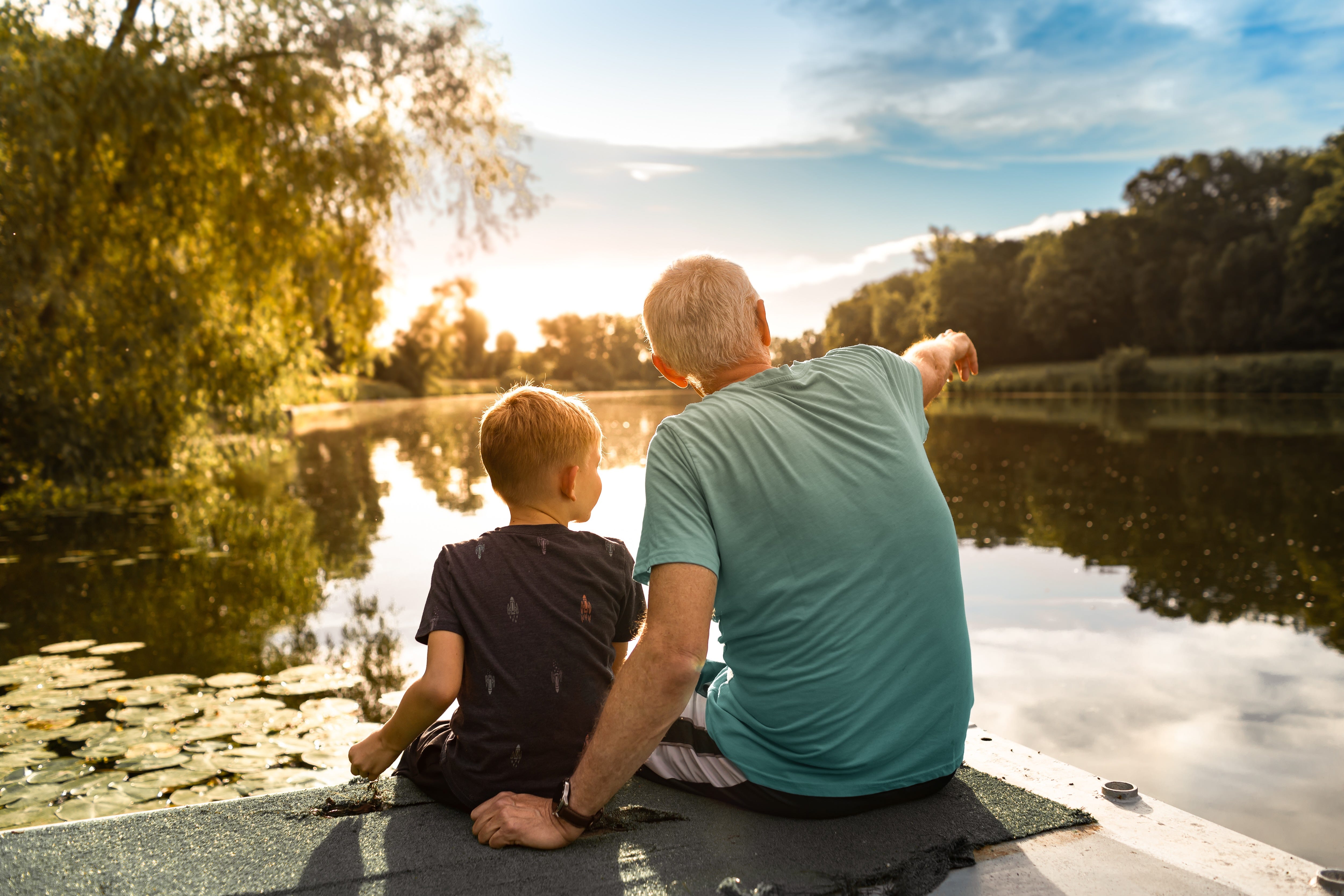 A grandfather sitting on a dock with his grandson.