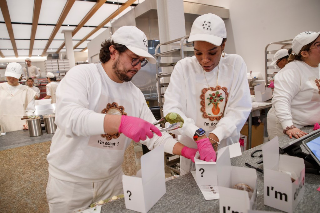 Workers pack up donuts into small white boxes with a question mark and 