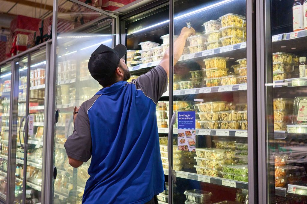 A worker stocks a grocery fridge. 