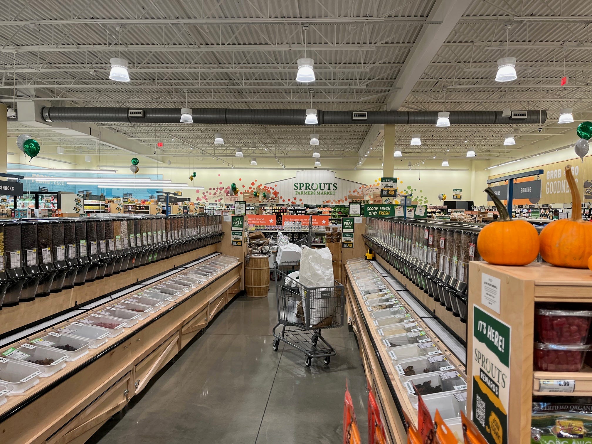 An aisle of bulk grains, nuts, and other dry groceries at Sprouts with a cart sitting in the middle.