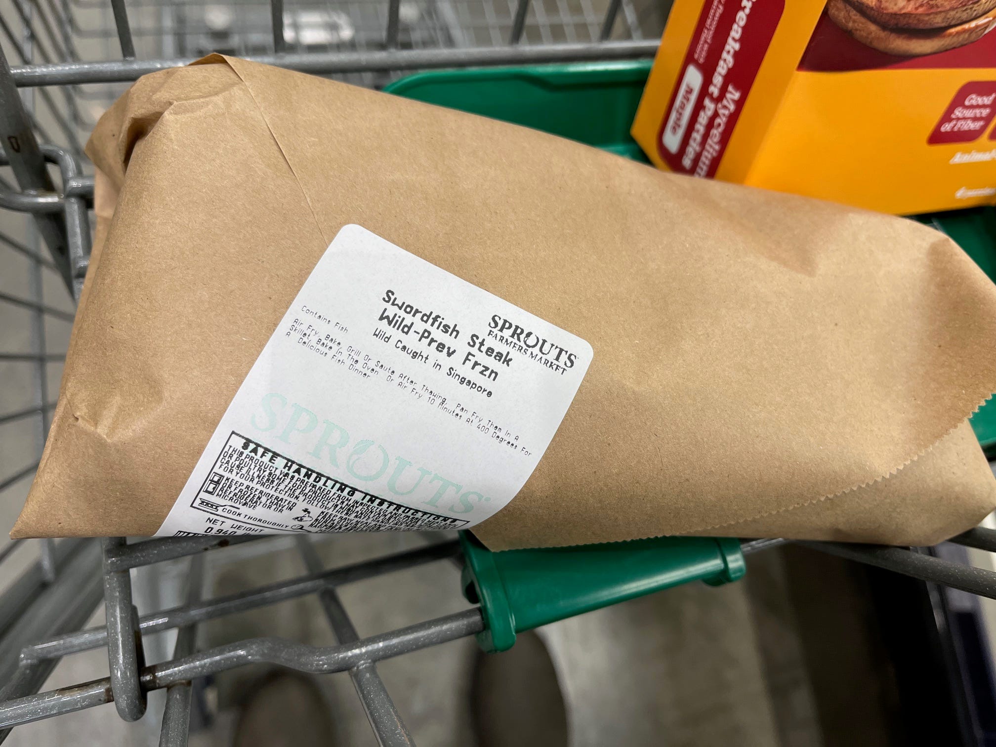 A Swordfish steak sits wrapped in brown paper in a shopping cart at Sprouts