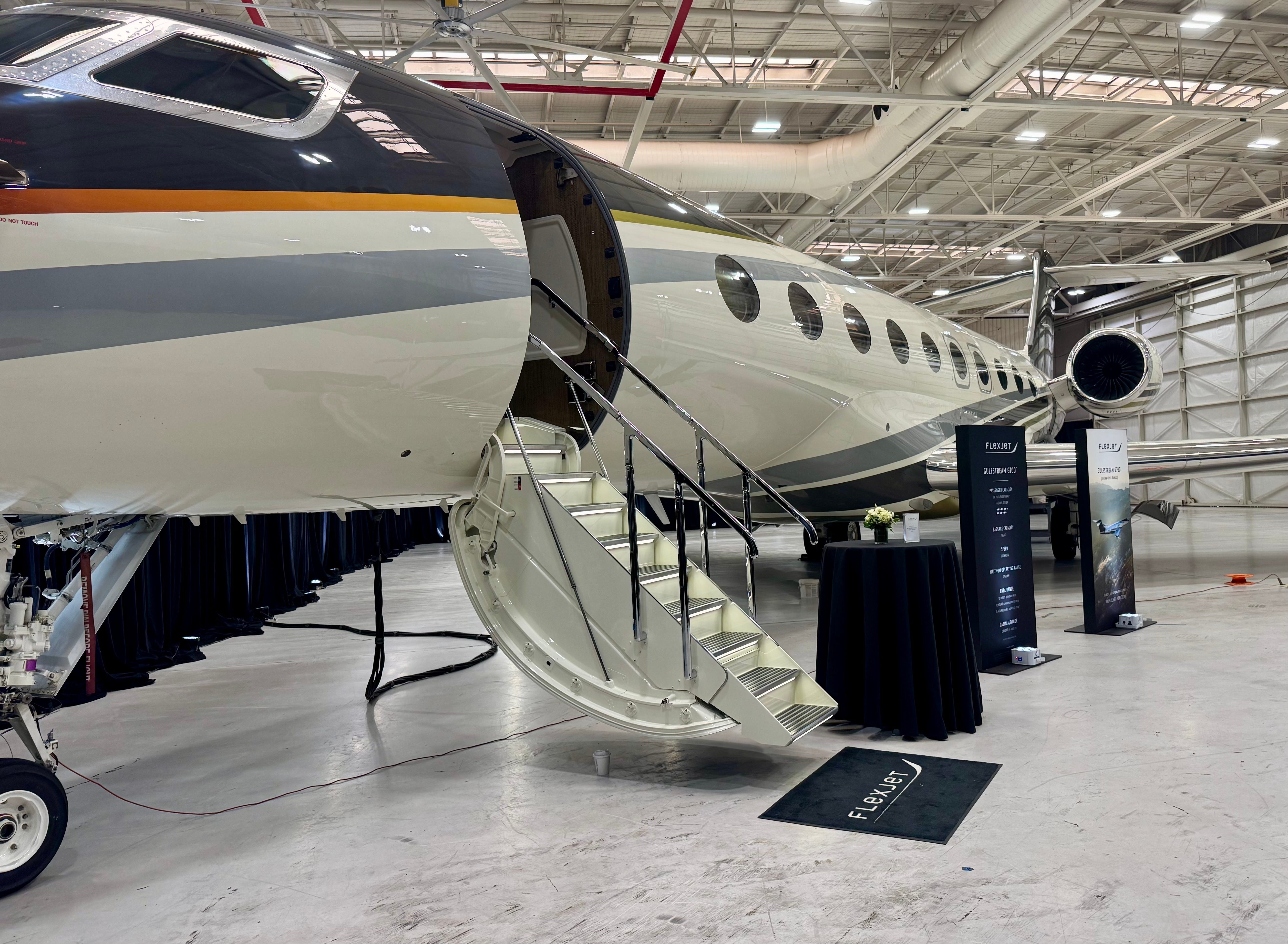 A picture of the Flexjet G700 in a hangar. Its white with gray and orange stripes.