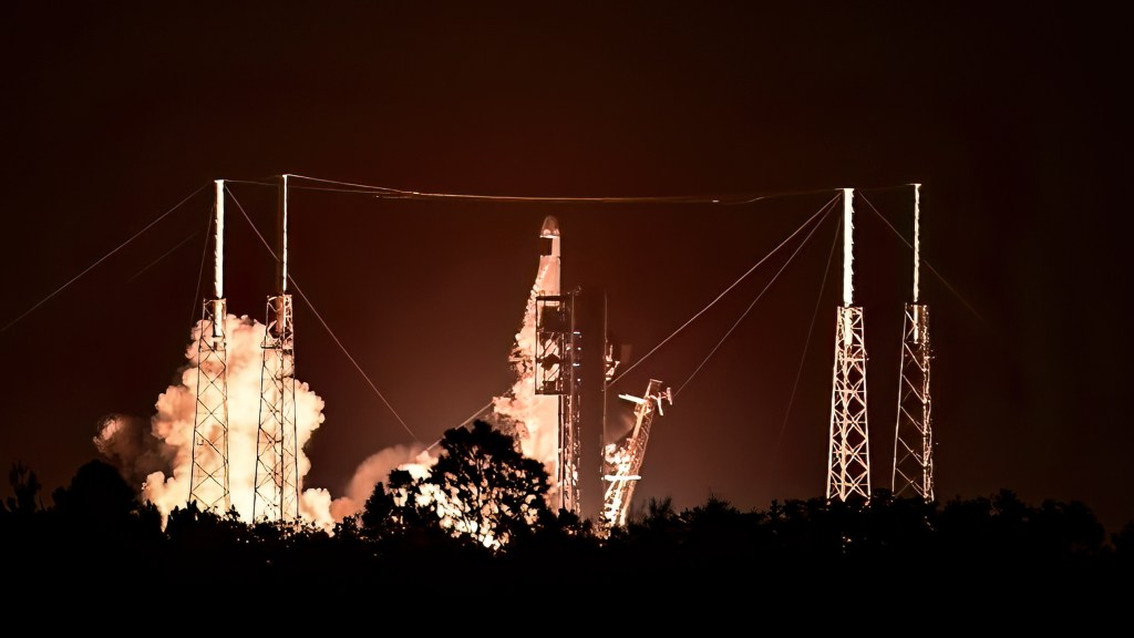 SpaceX Falcon 9 rocket launching at night, illuminated by flames and smoke.