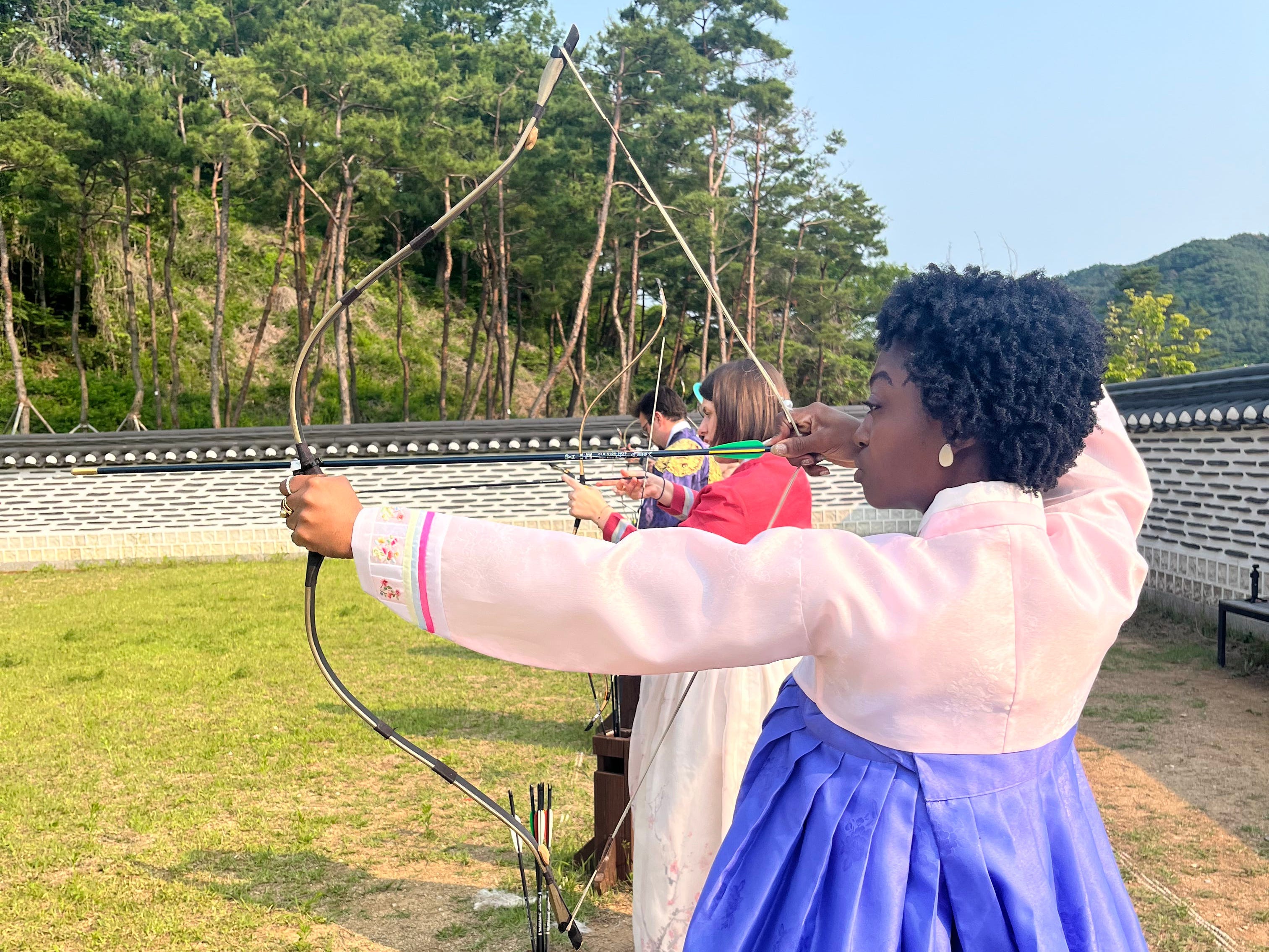 A woman trying out archery while dressed in a hanbok in Korea.