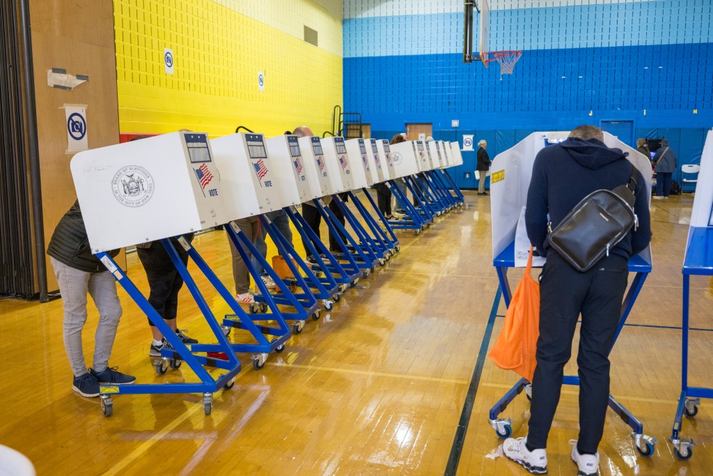 People voting at polling booths in a gymnasium.