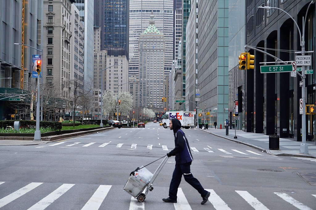 A pedestrian pulling a cart crosses an empty Park Avenue at 57th Street in New York City.