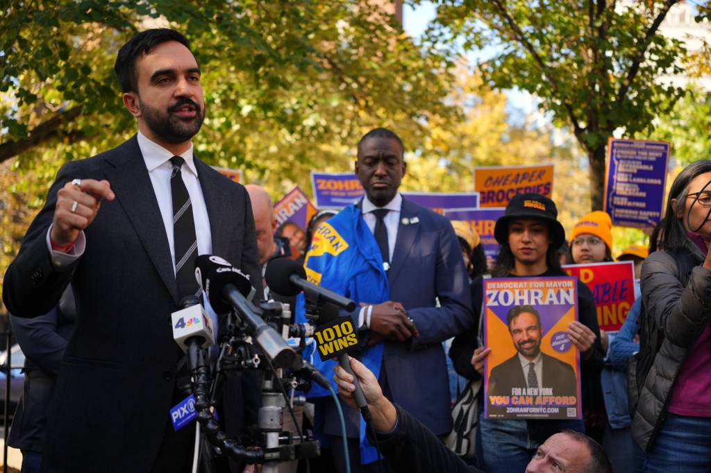 Zohran Mamdani speaks at a canvass launch in Harlem, with supporters holding campaign signs for him.